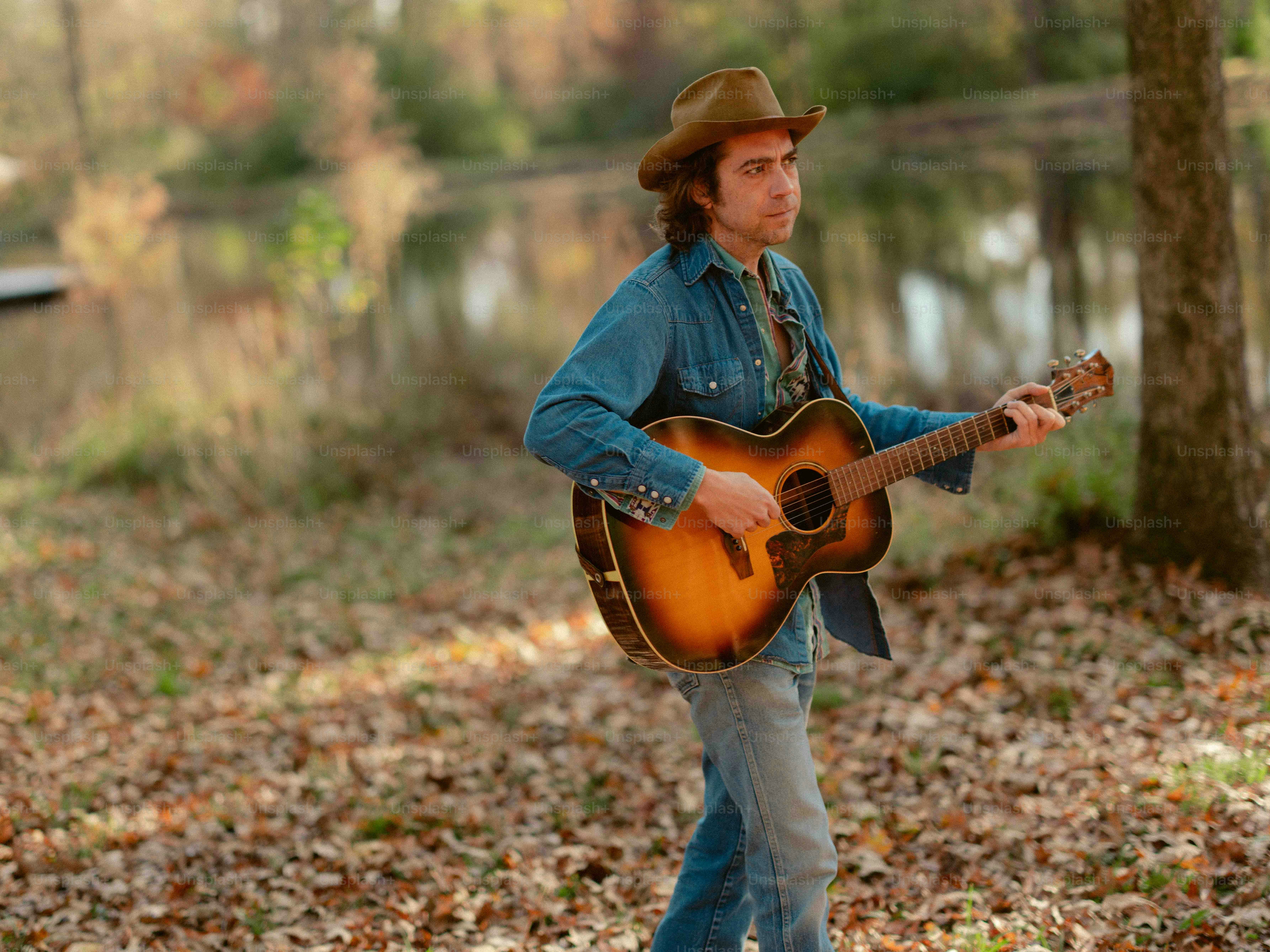 A man with a hat playing a guitar in the woods