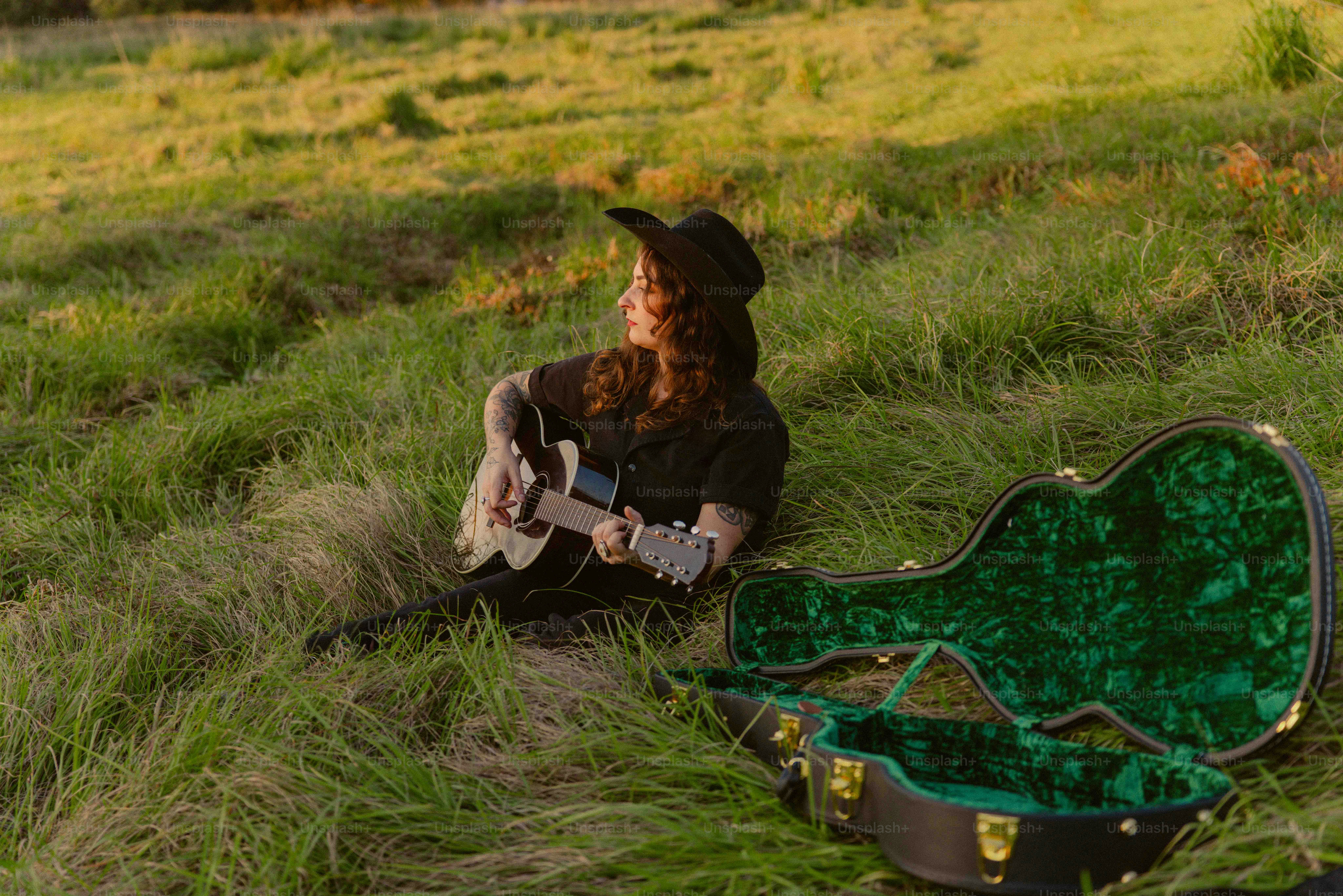 A man sitting in a field with a guitar