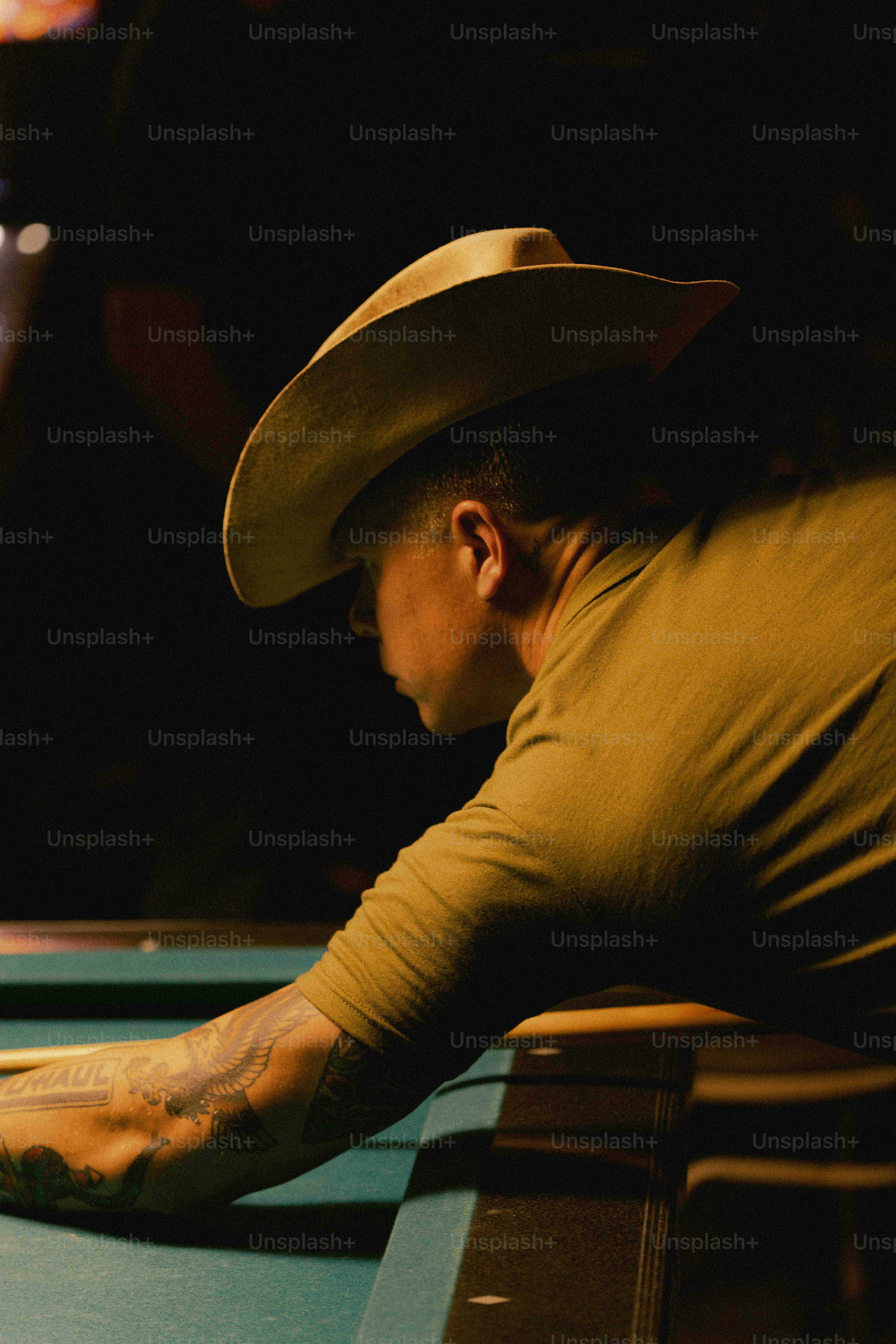 A man in a cowboy hat leaning over a pool table