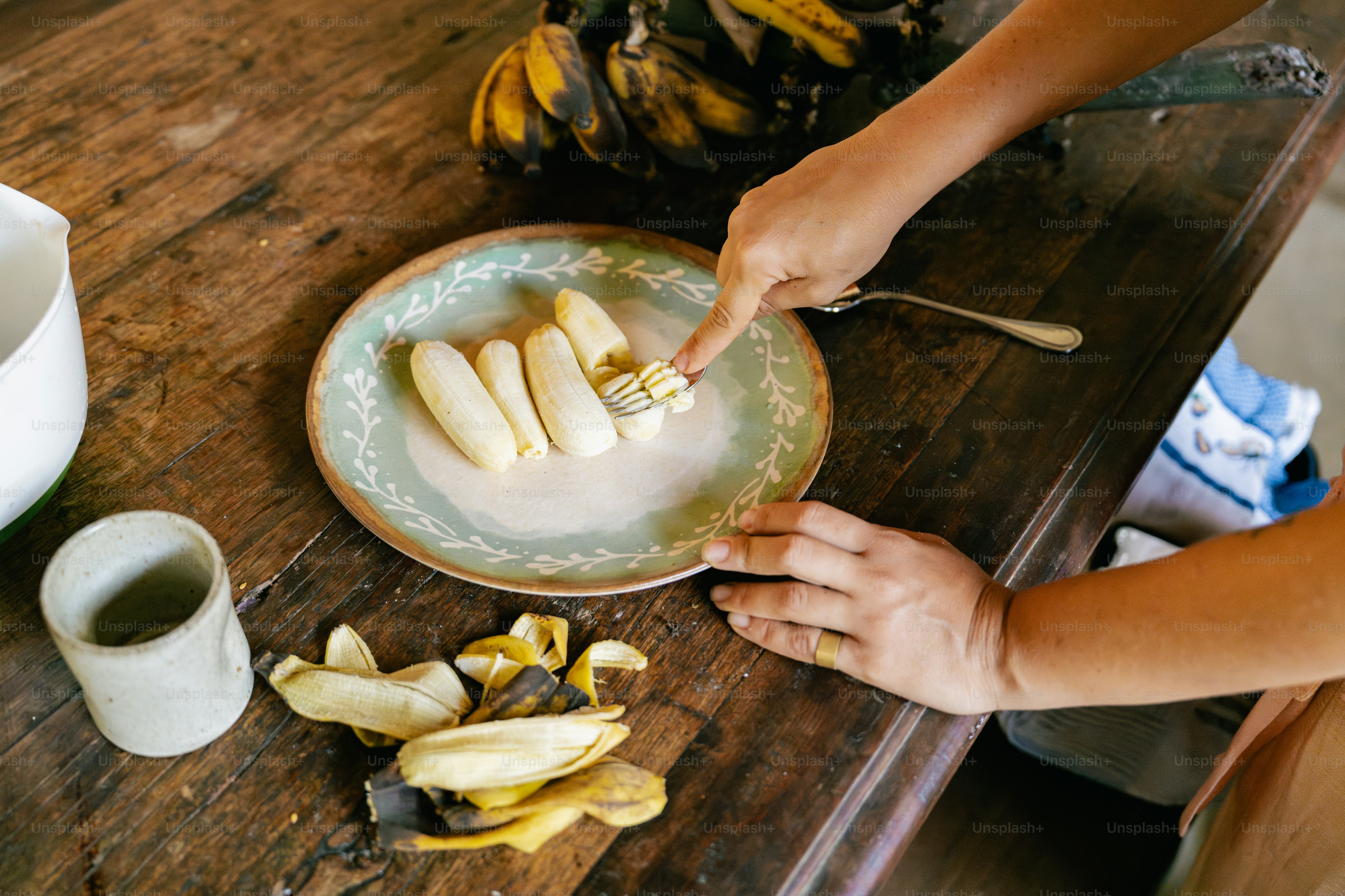 A person cutting bananas on a plate on a table