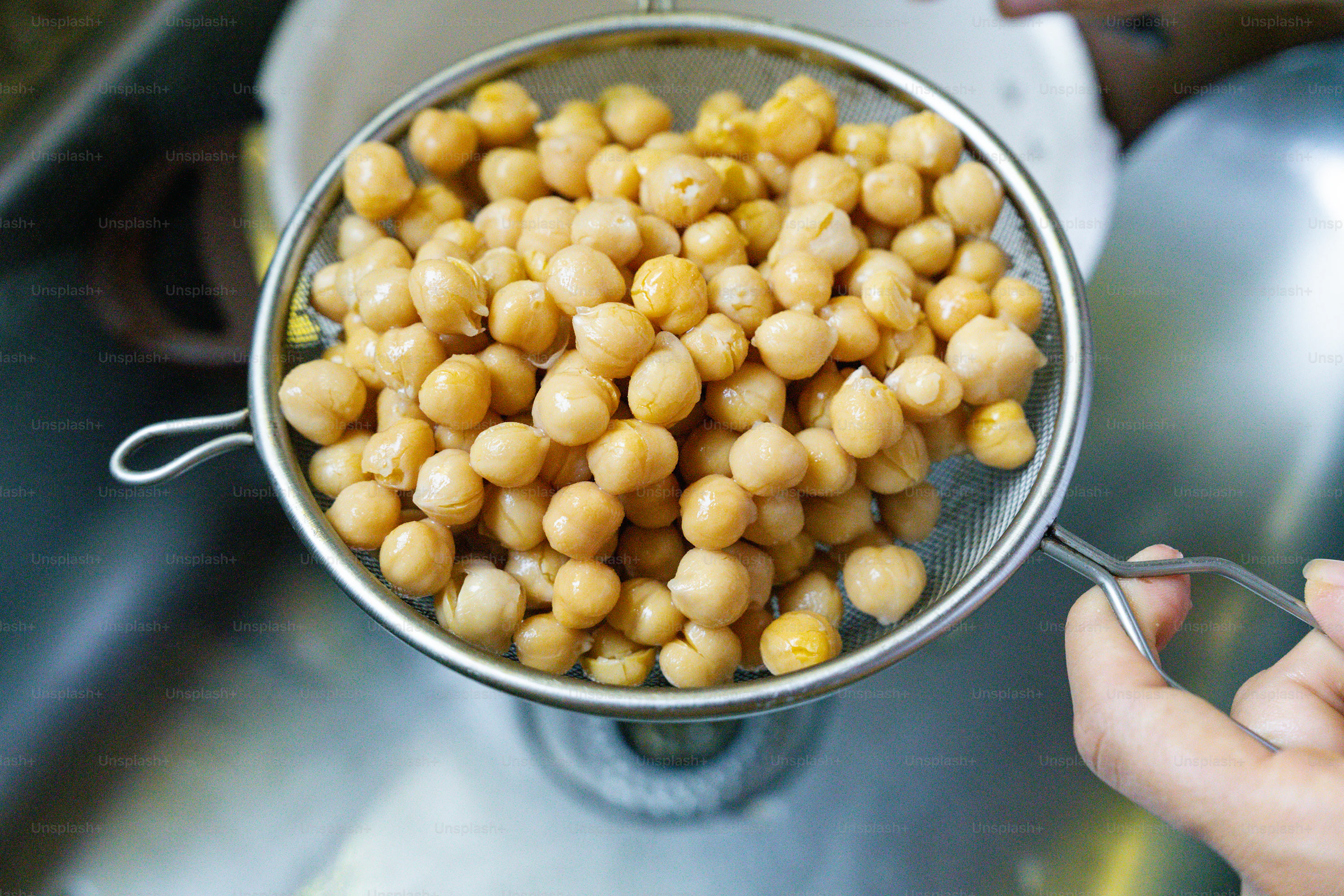 A person holding a metal bowl filled with chickpeas