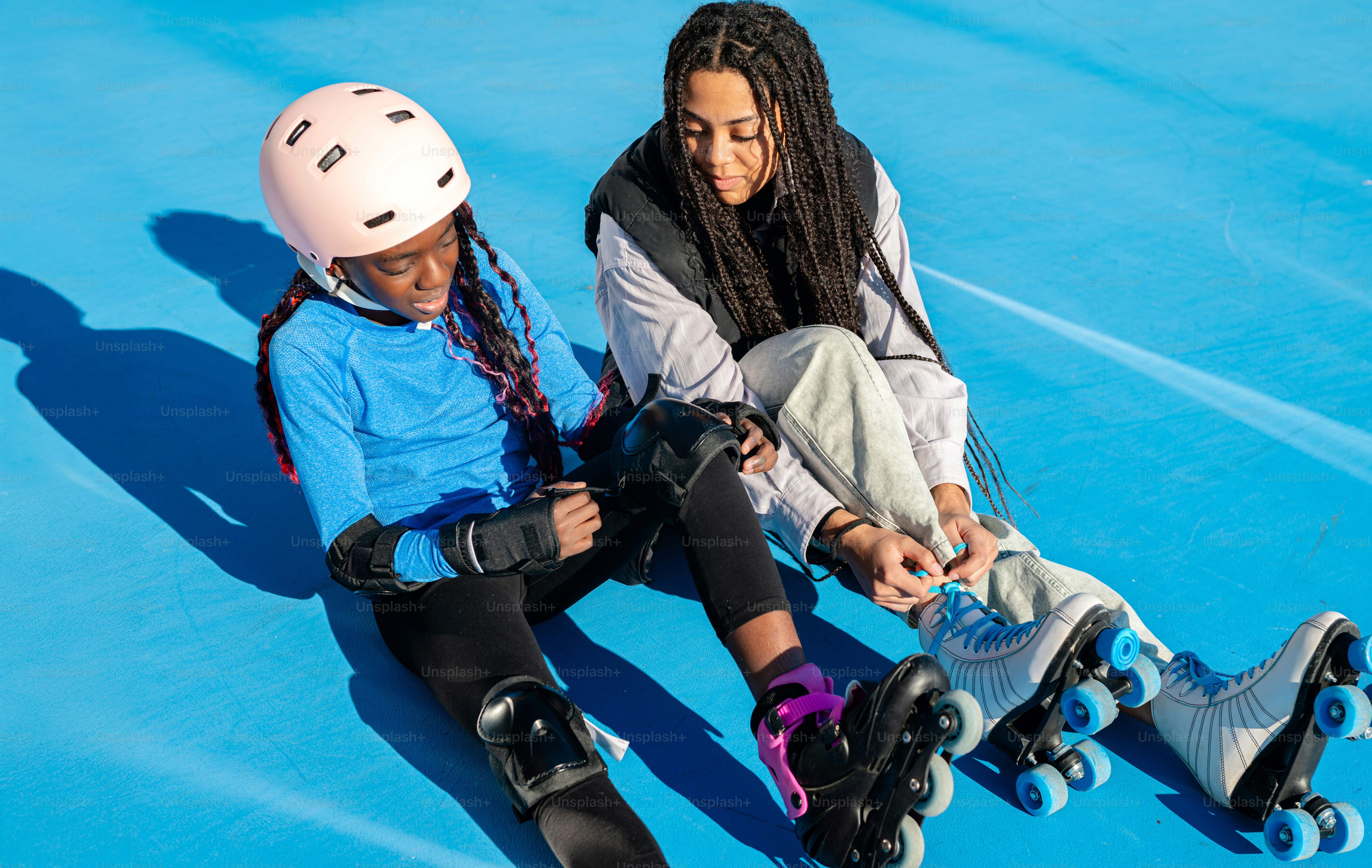 Two girls sitting on skateboards on a blue surface