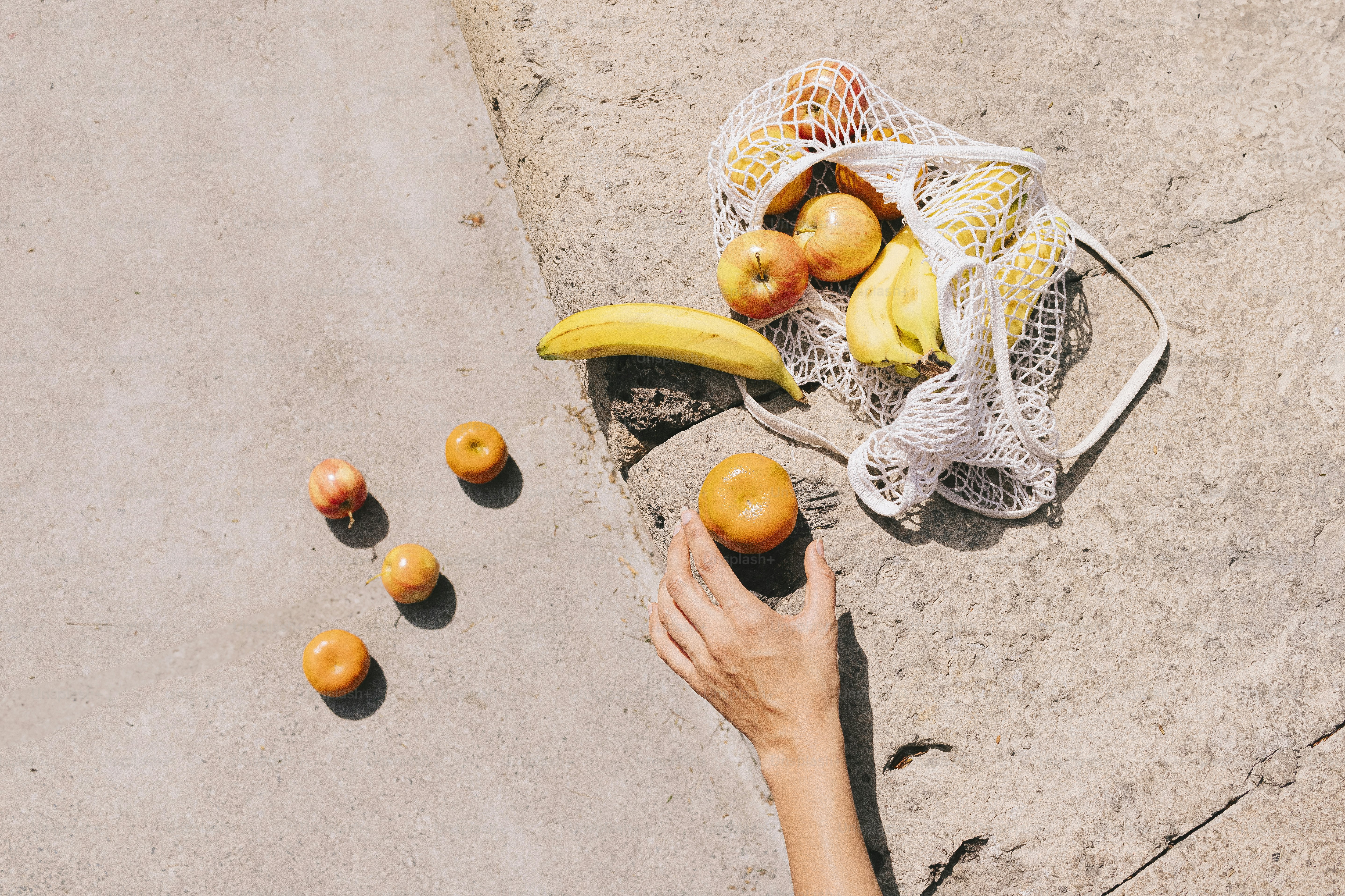 A person holding a bag of oranges next to a bunch of bananas