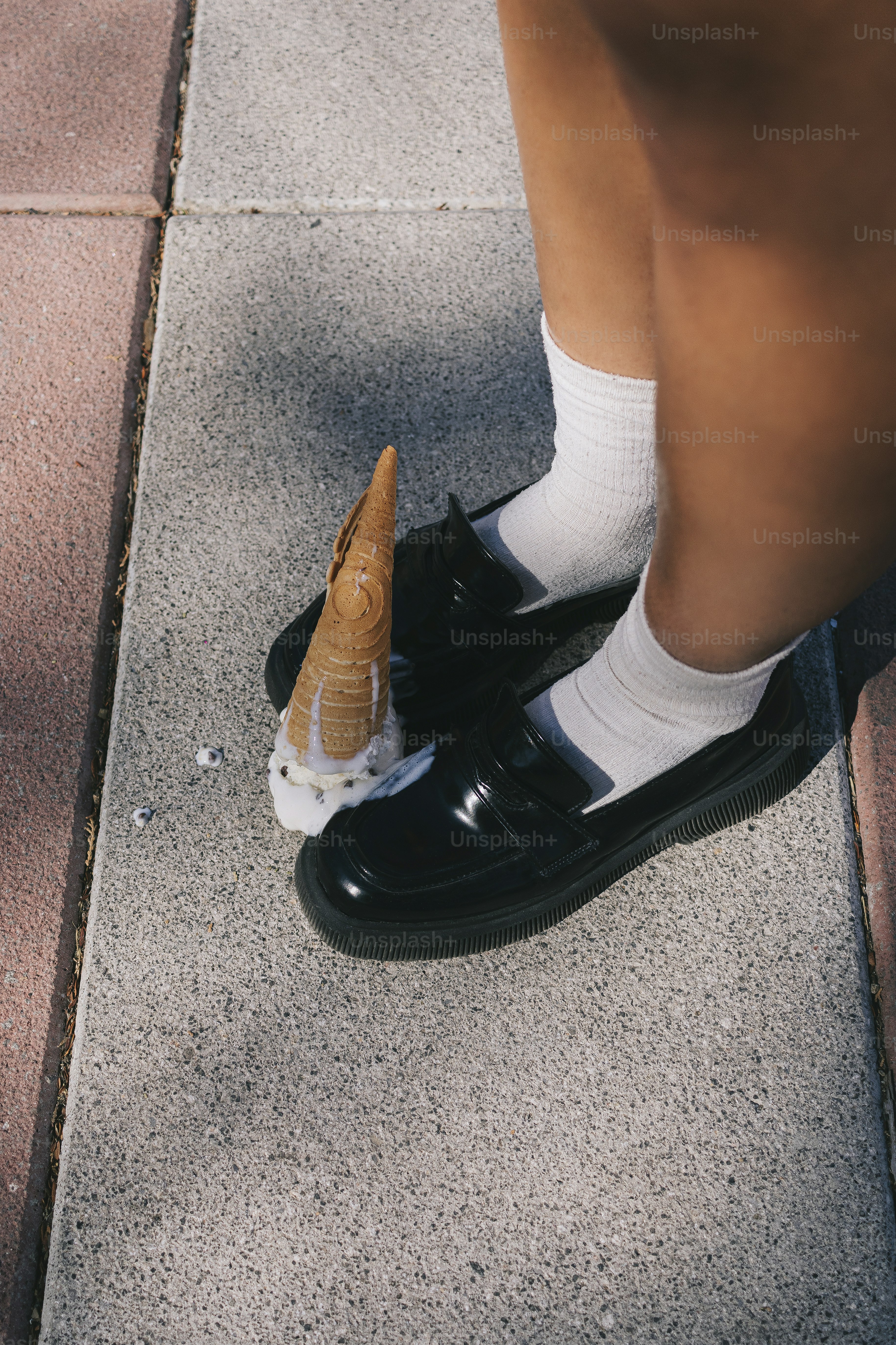 A person standing on a sidewalk with an ice cream cone in their shoe