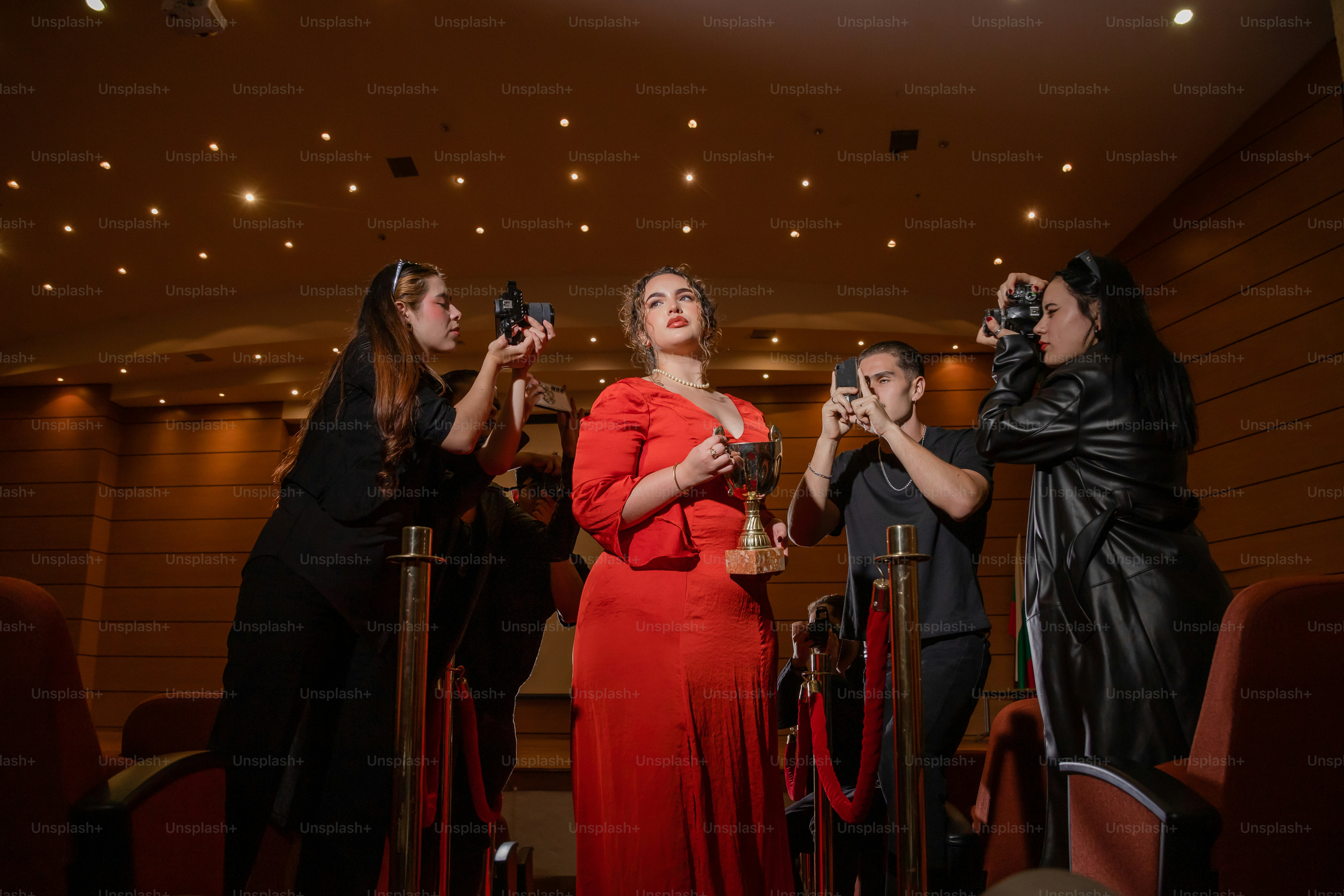 A group of people taking pictures of a woman in a red dress