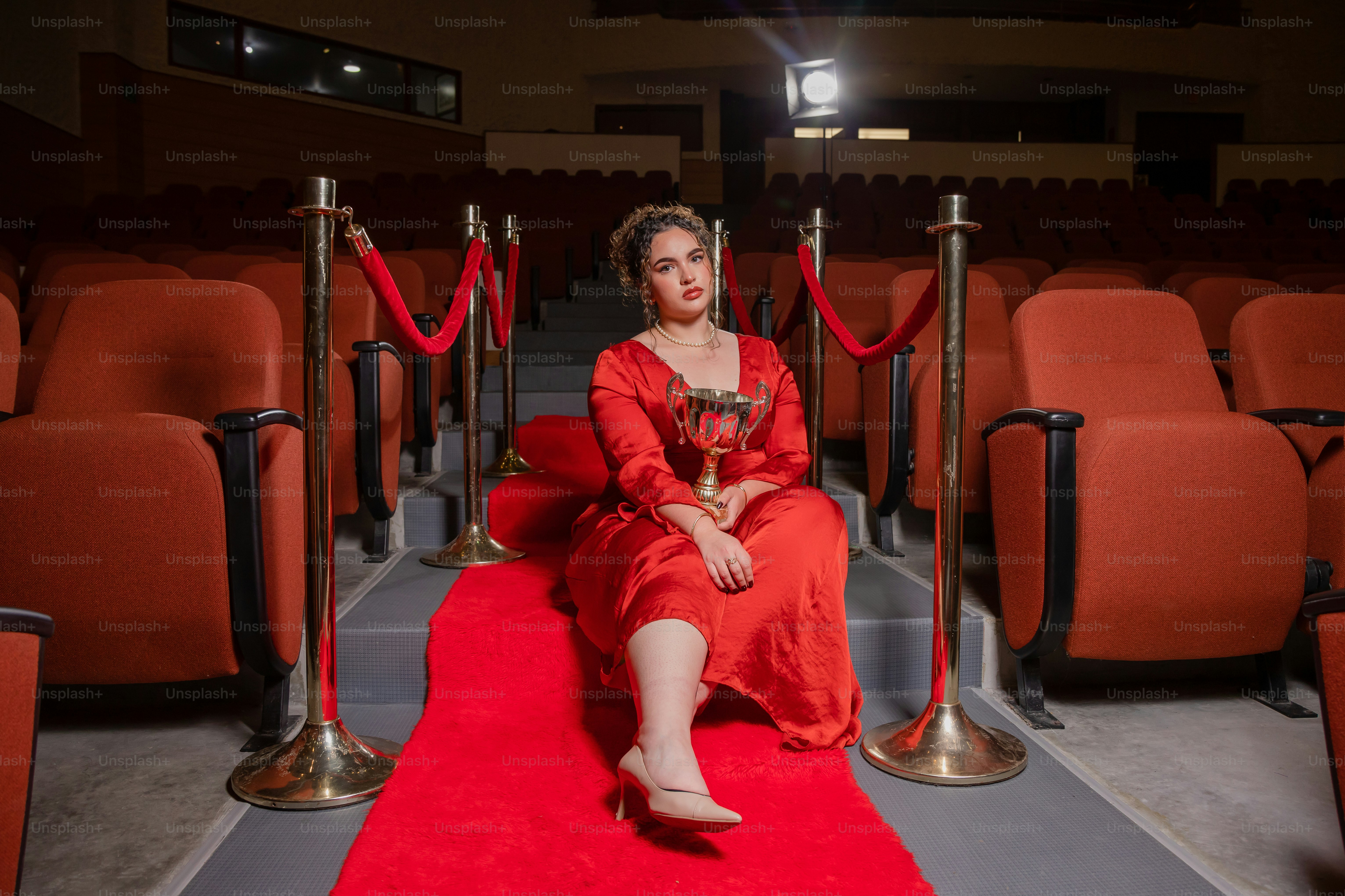 A woman in a red dress sitting on a red carpet photo – Celebration ...