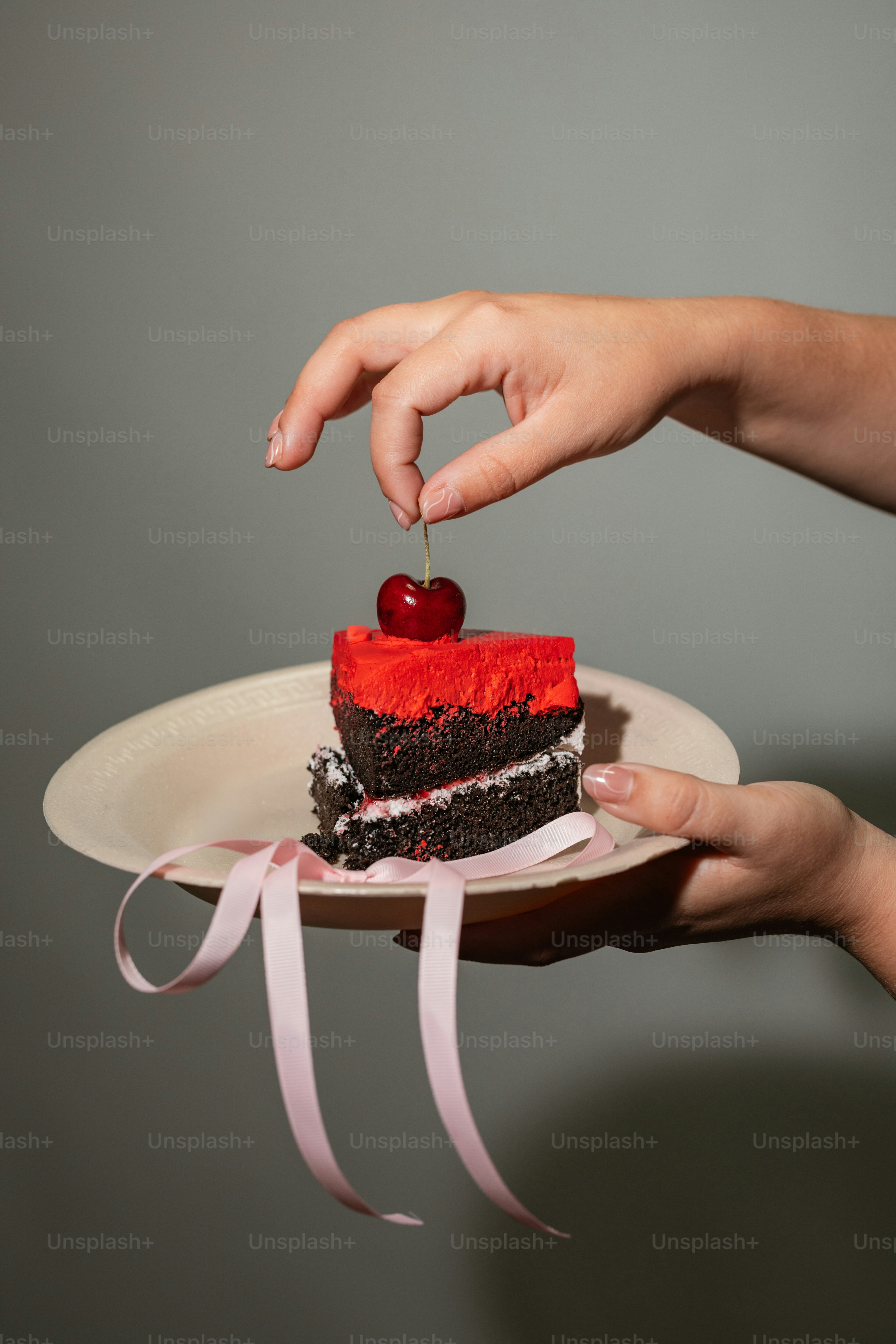 A person holding a piece of cake with a cherry on top