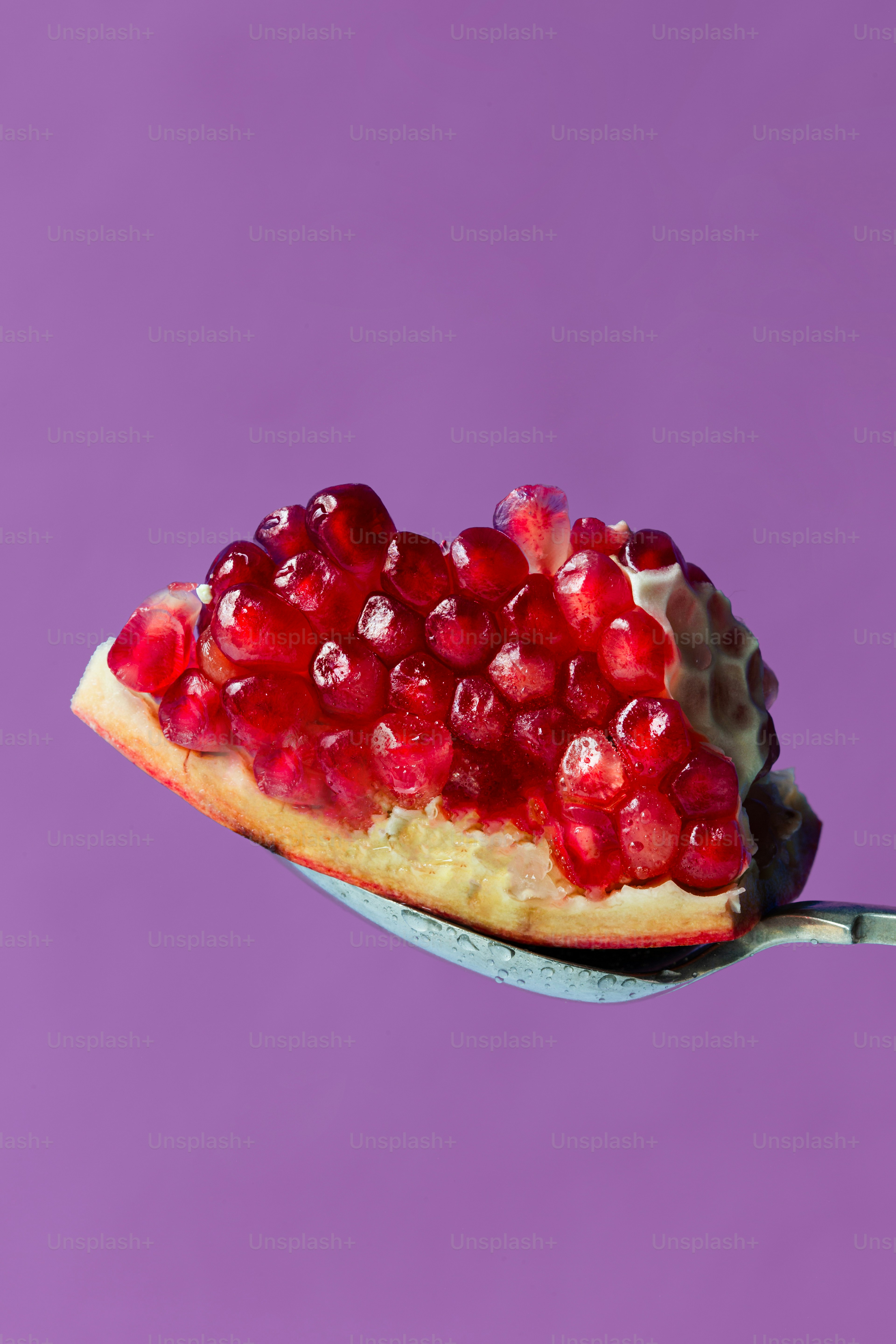 Una cuchara llena de granada sobre un fondo morado