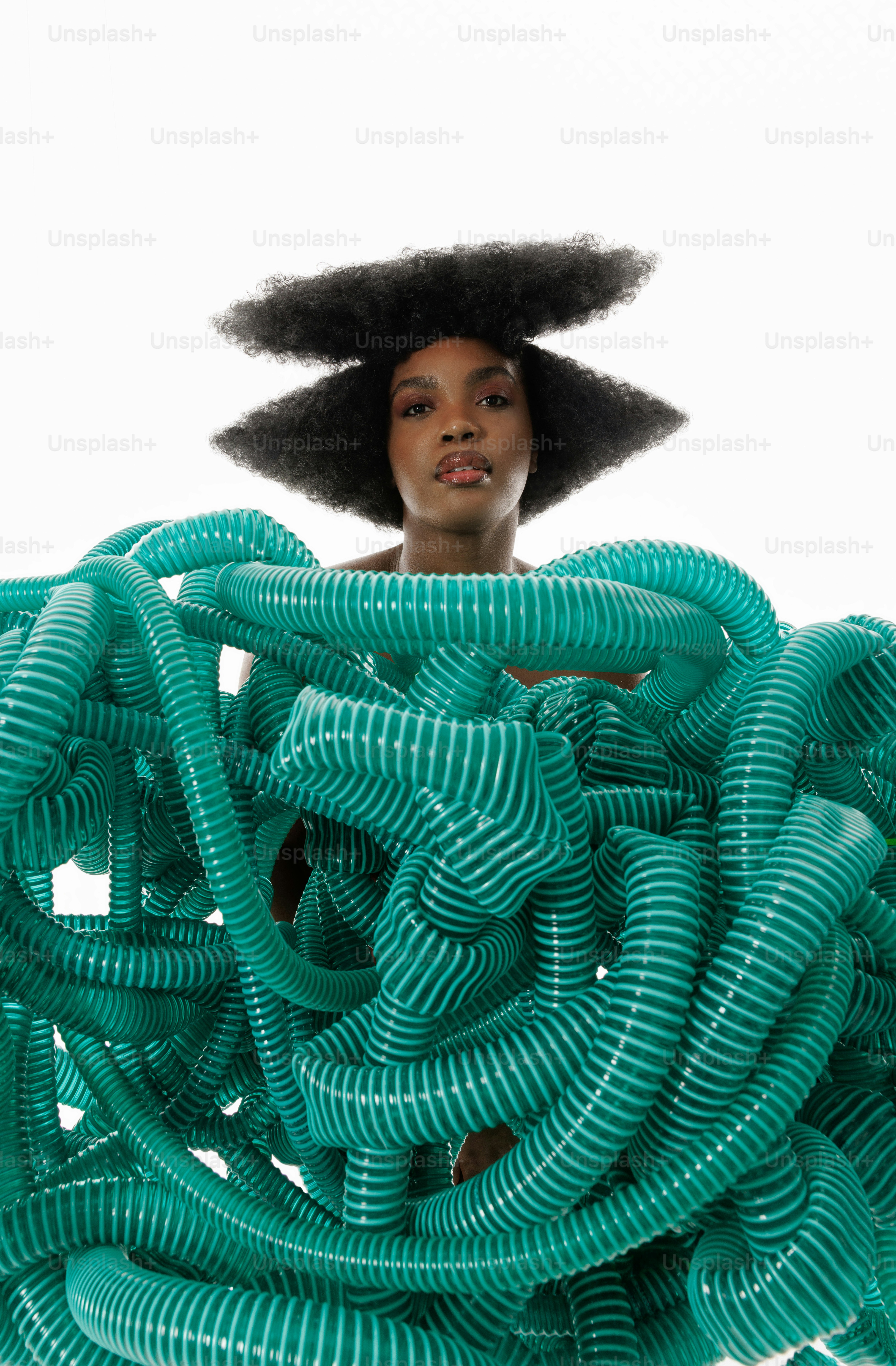 A woman with an afro standing behind a bunch of green hoses