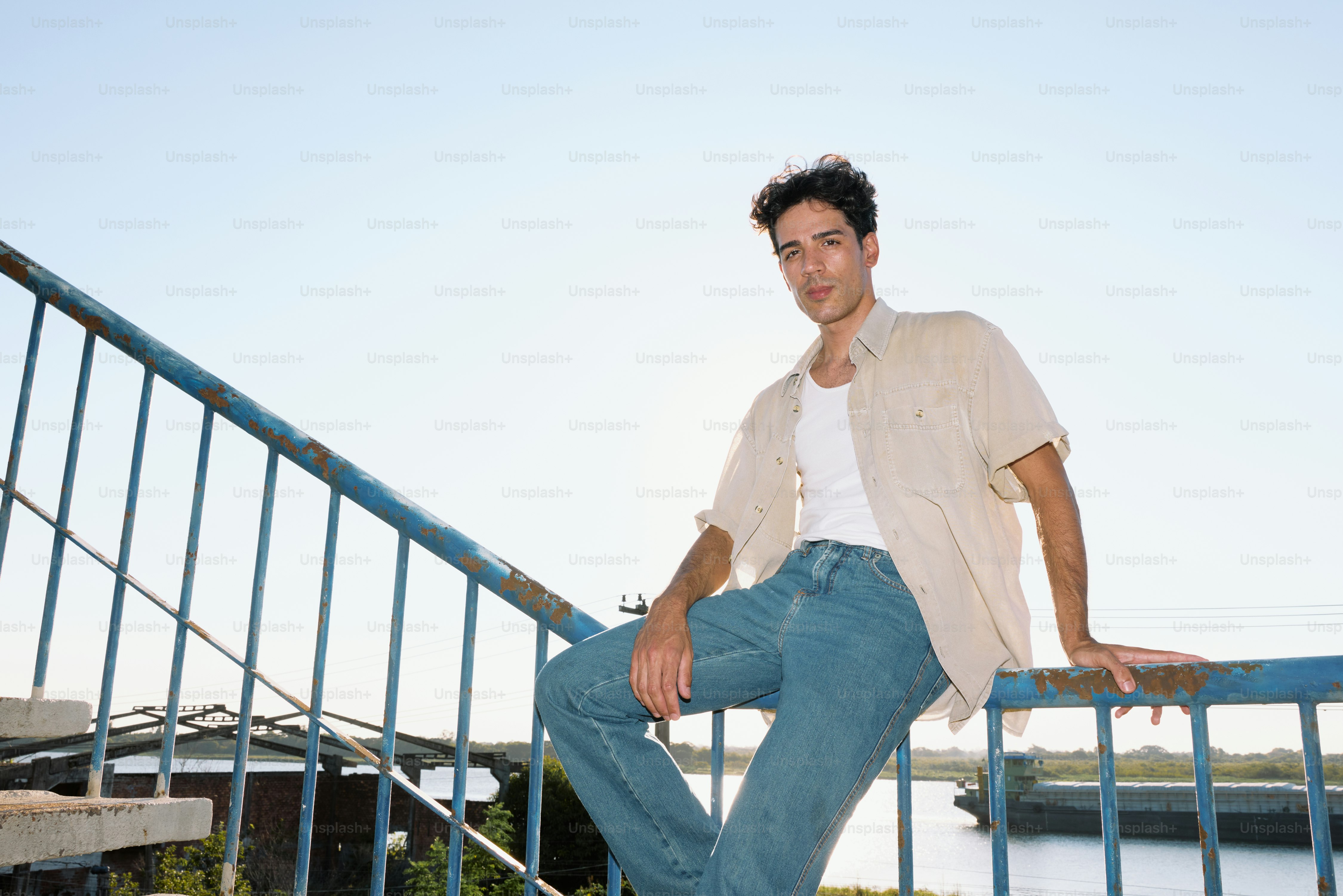A man leaning on a railing next to a body of water photo – Portrait ...