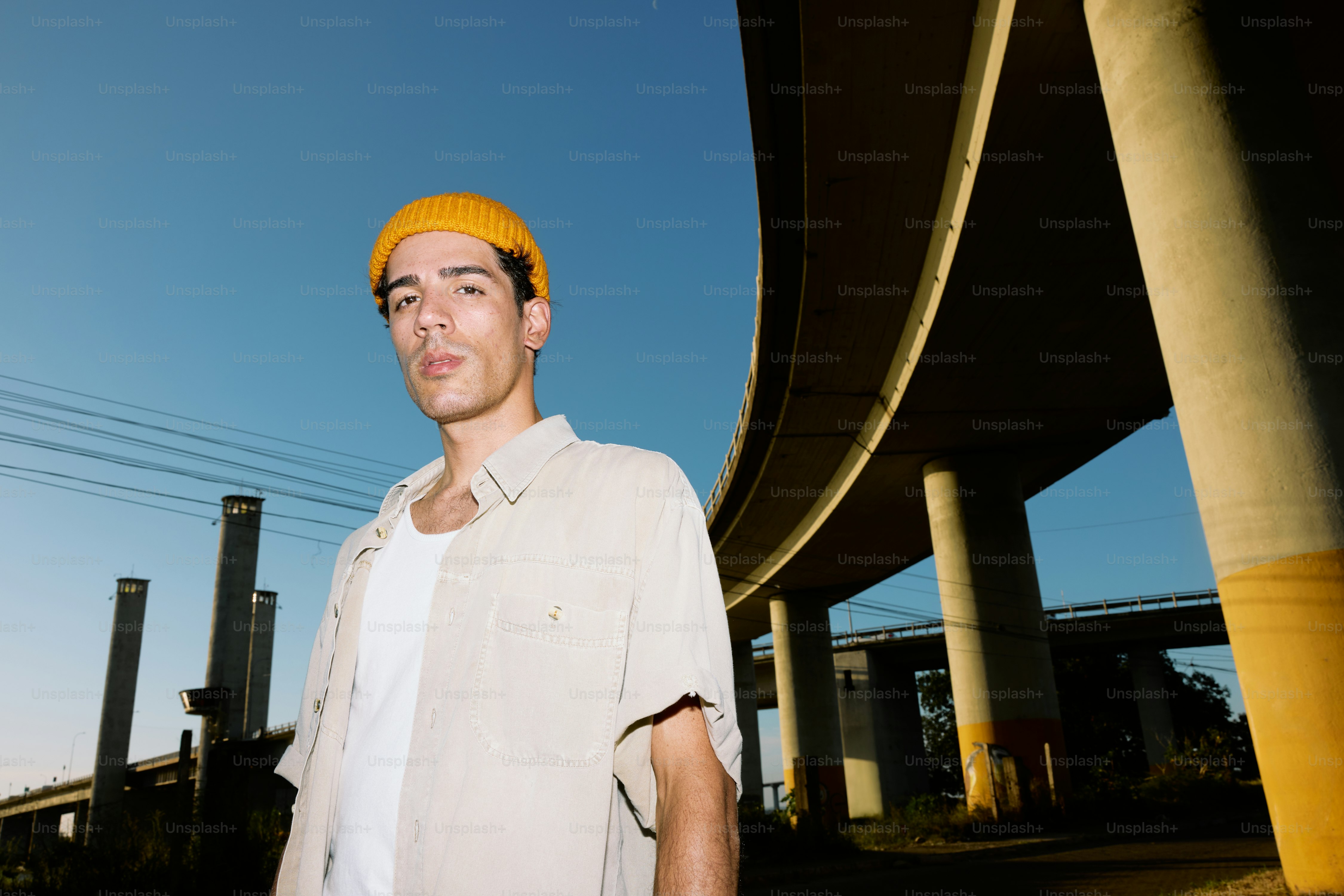 A man standing in front of a bridge wearing a yellow hat