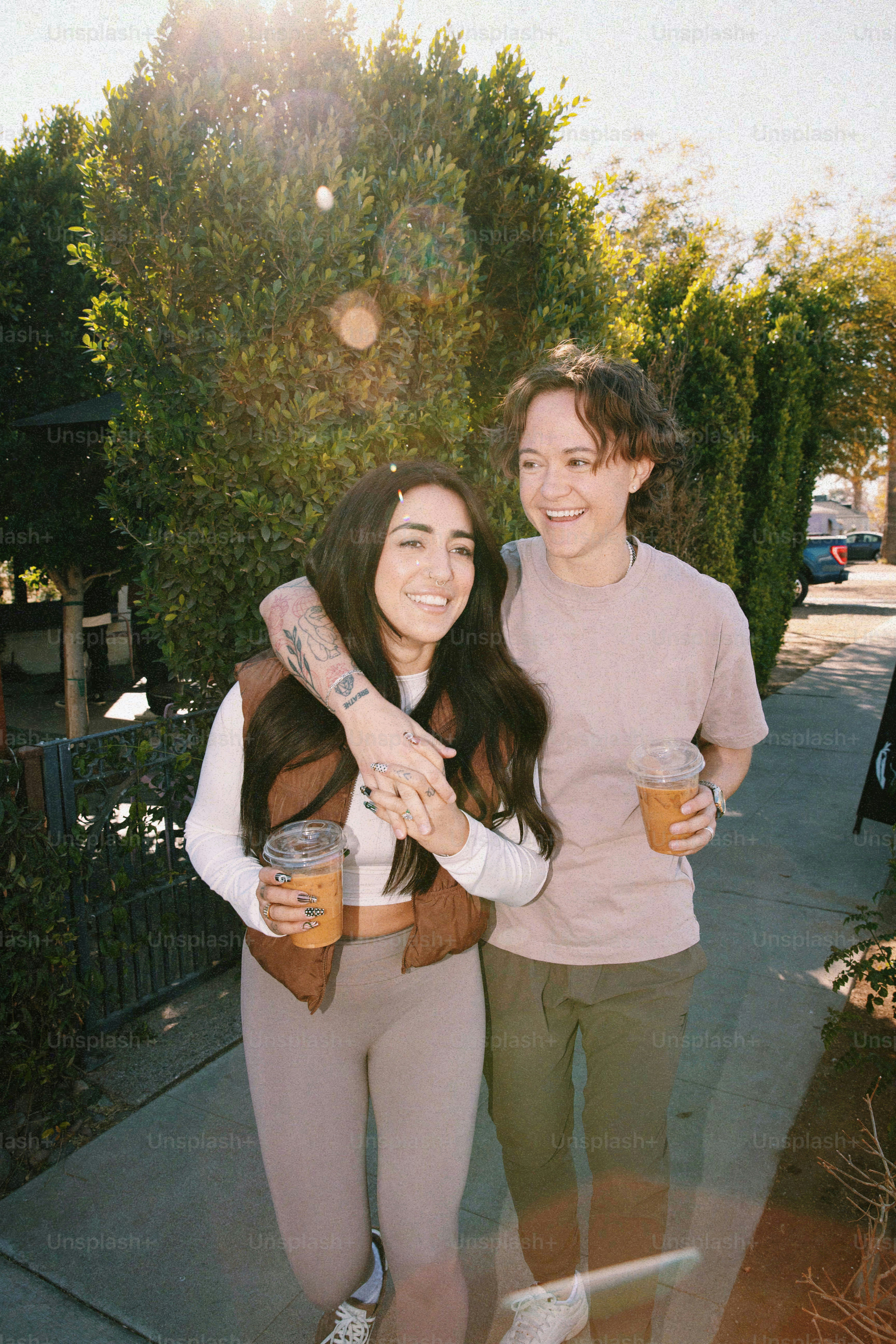 Two friends laugh and walk with drinks.