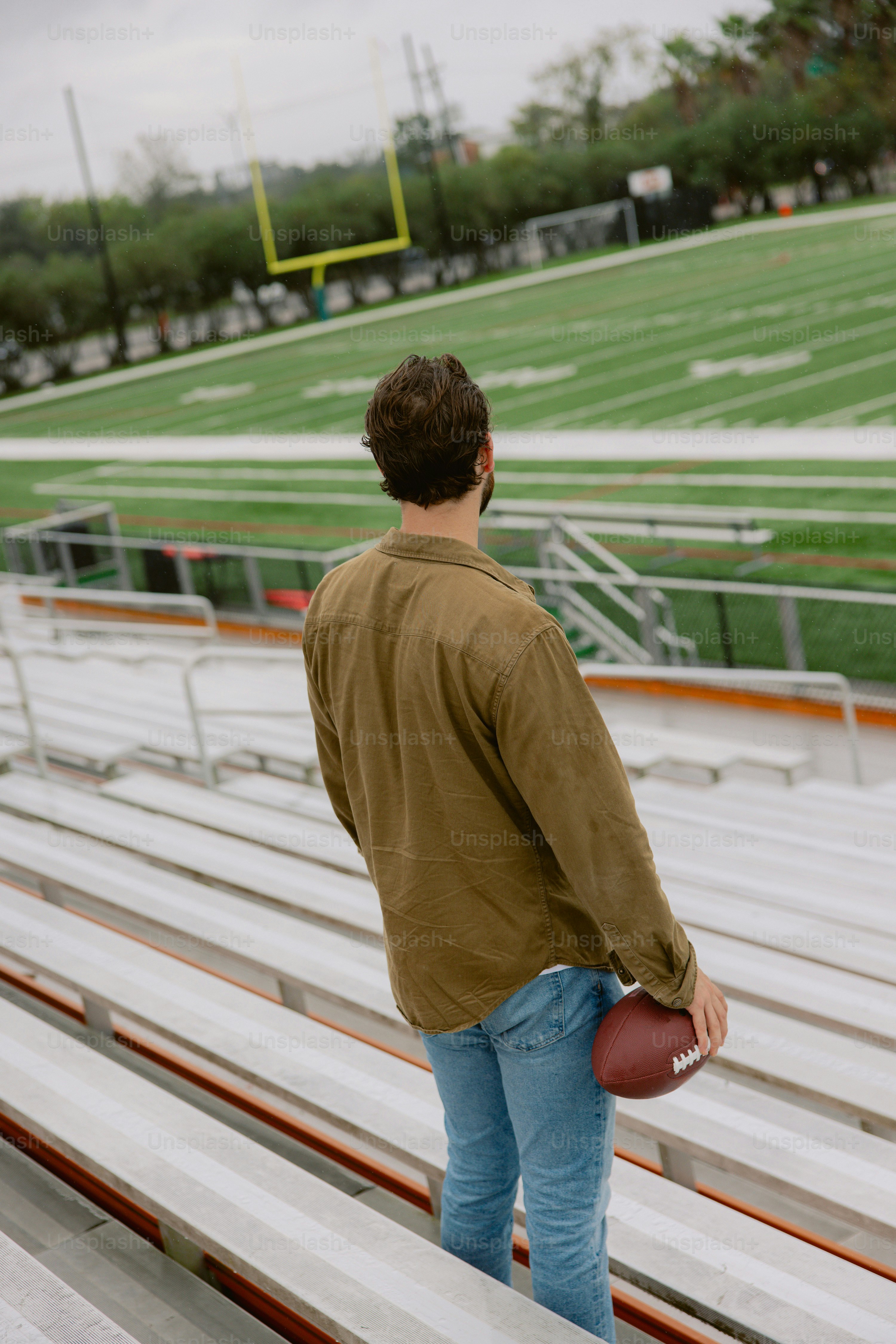 Um homem em pé em uma arquibancada segurando uma bola de futebol