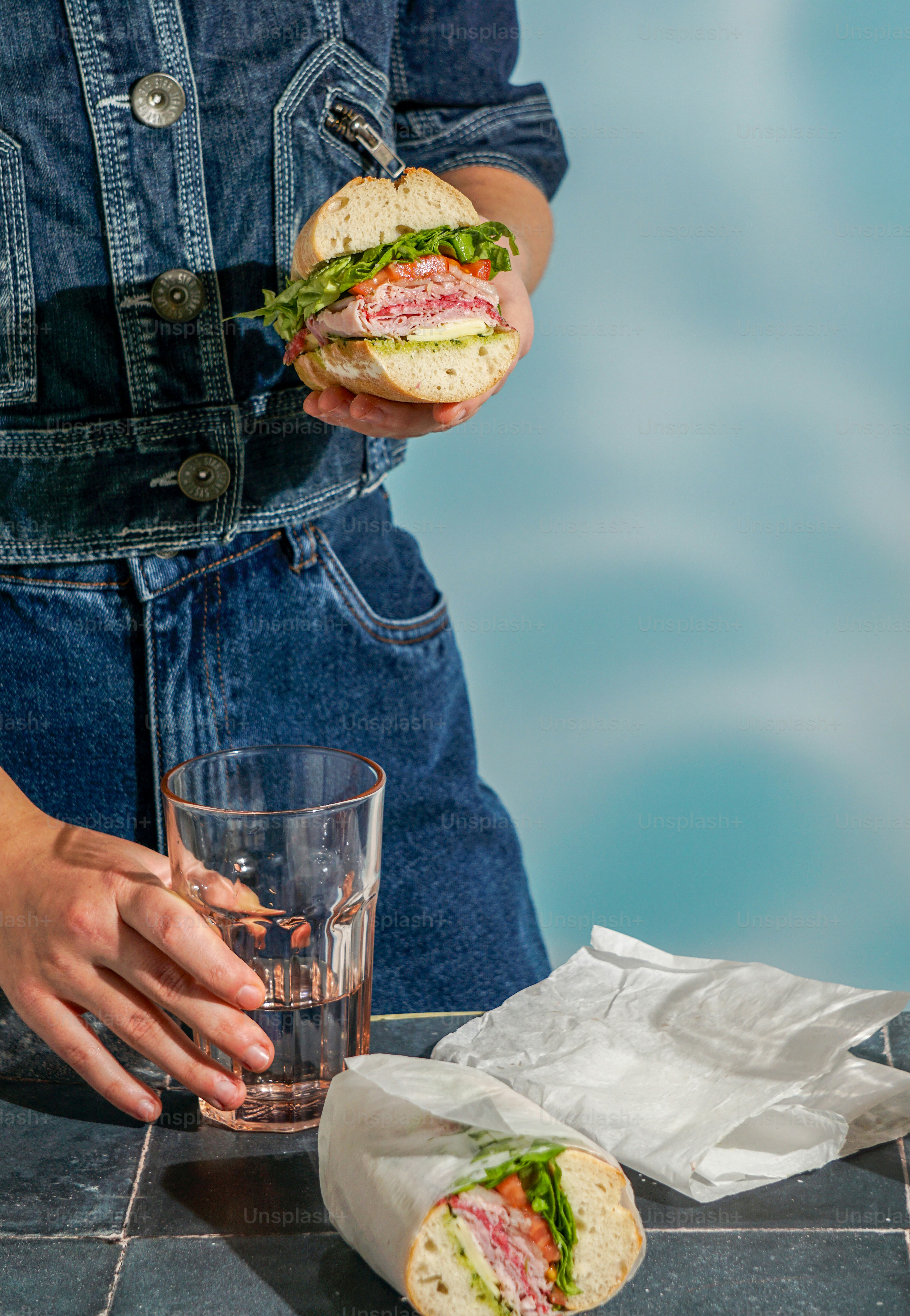A person holding a sandwich and a glass of water
