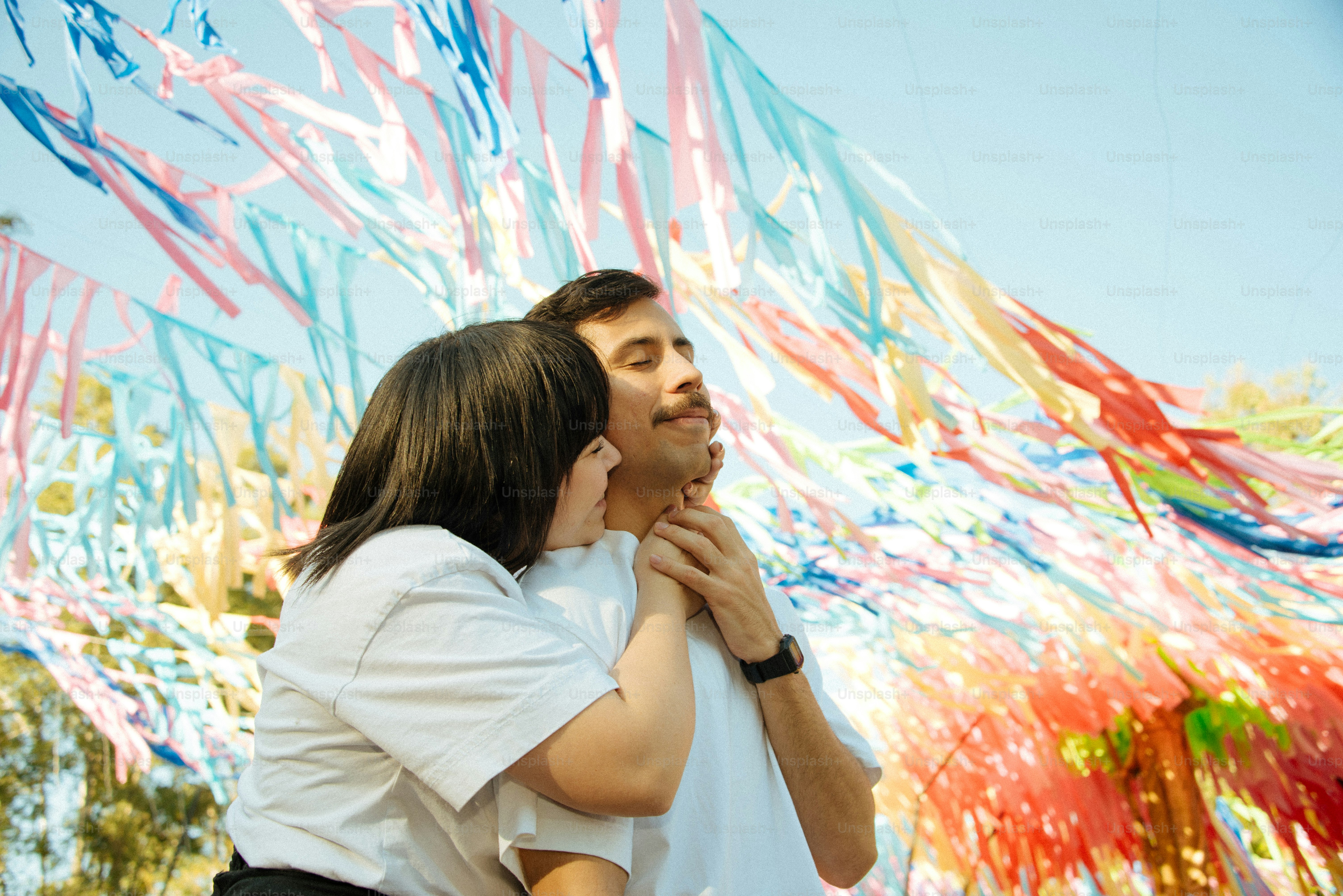 Couple embraces under colorful streamers in the sunlight.