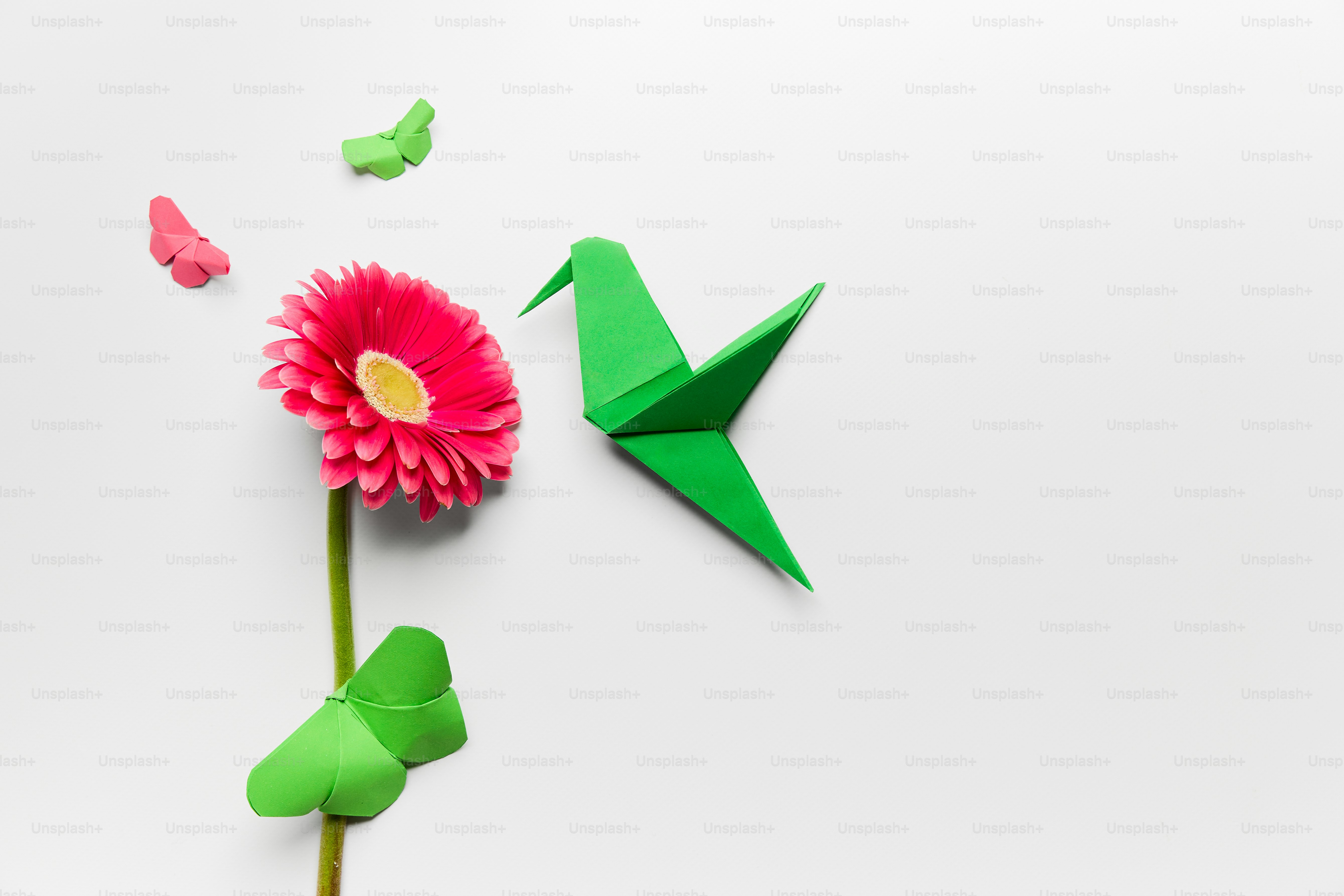 A flower and a green origami bird on a white background