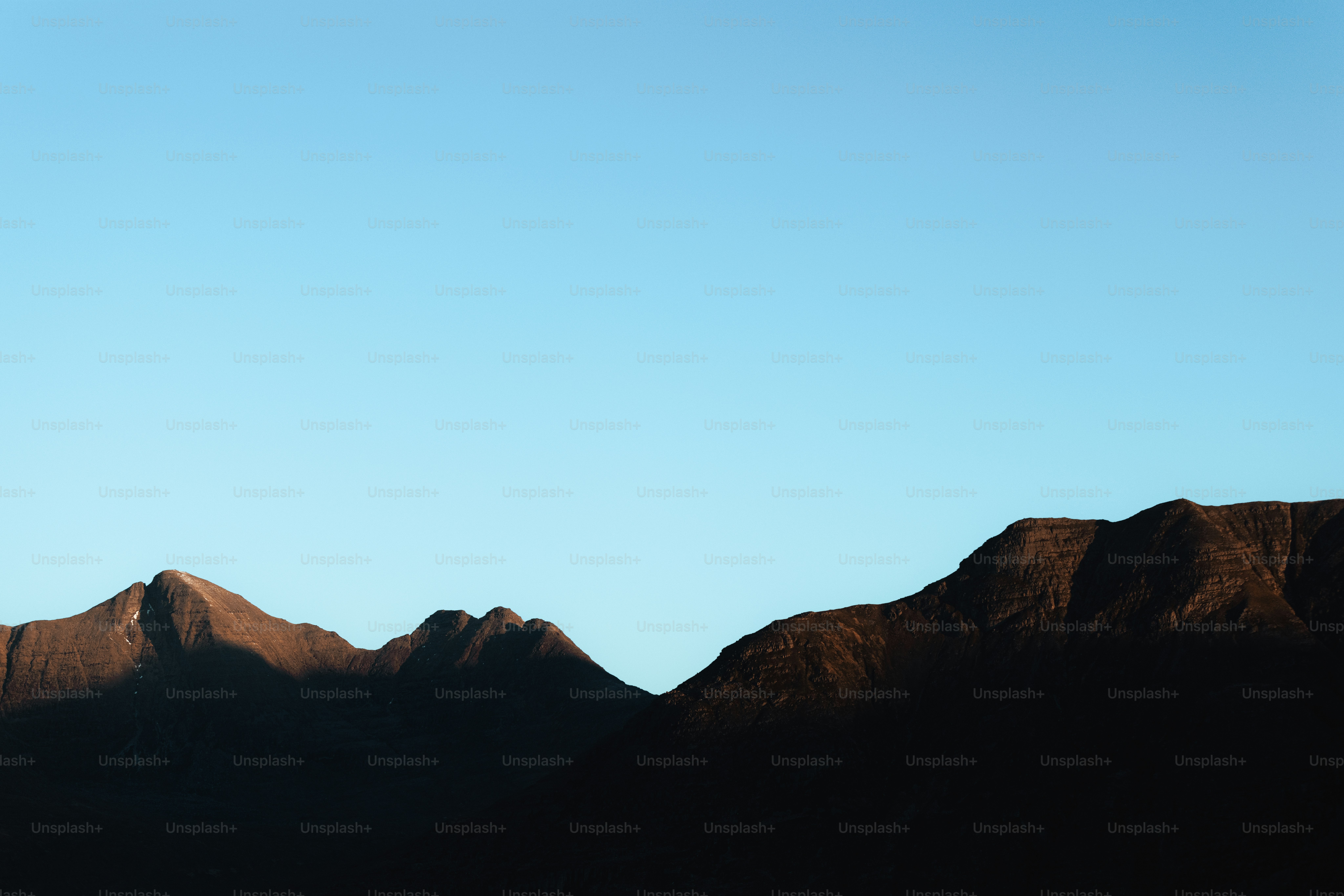 A plane flying over a mountain range with a blue sky in the background