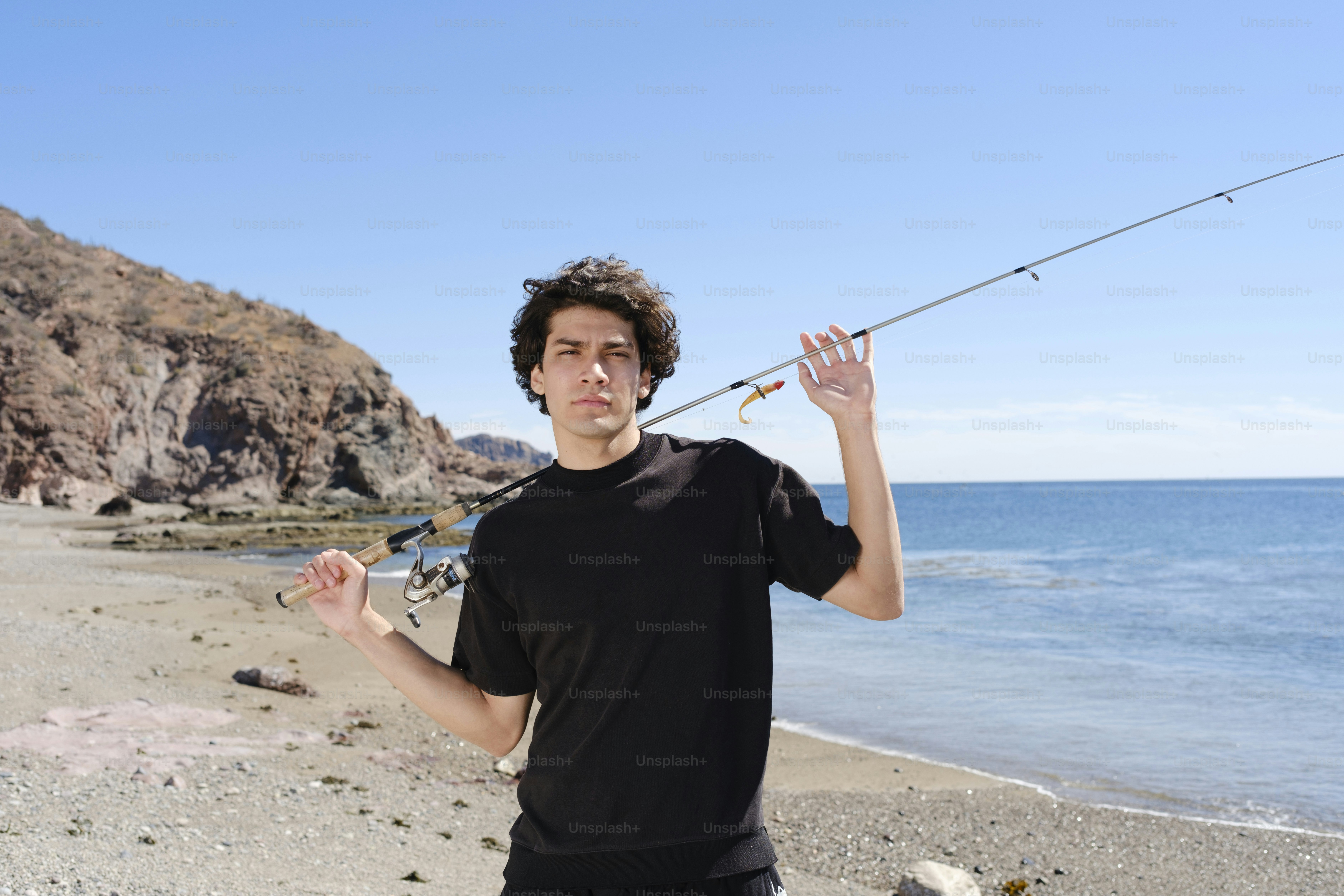 A man standing on a beach holding a fishing pole