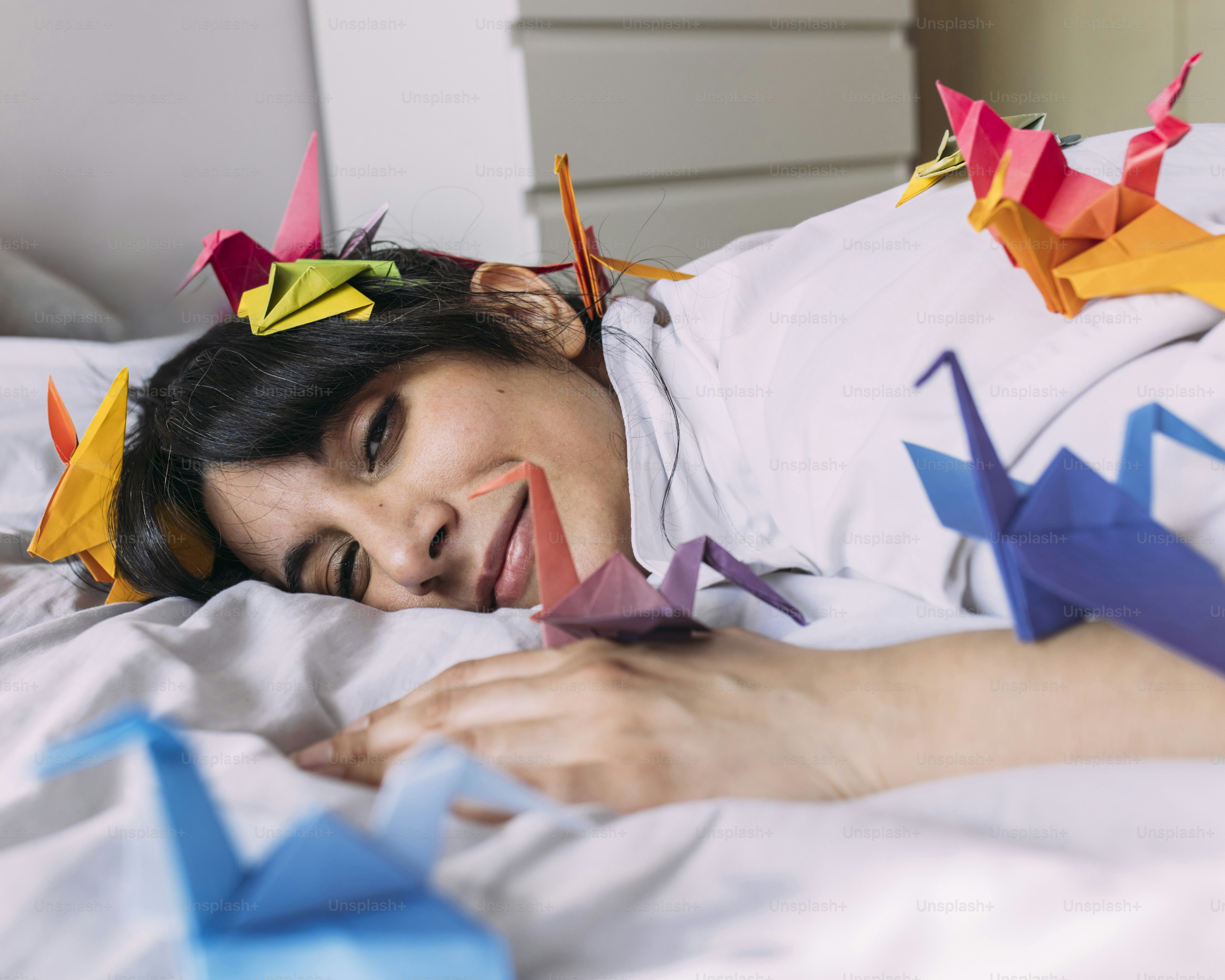 A woman laying in bed with origami birds on her head