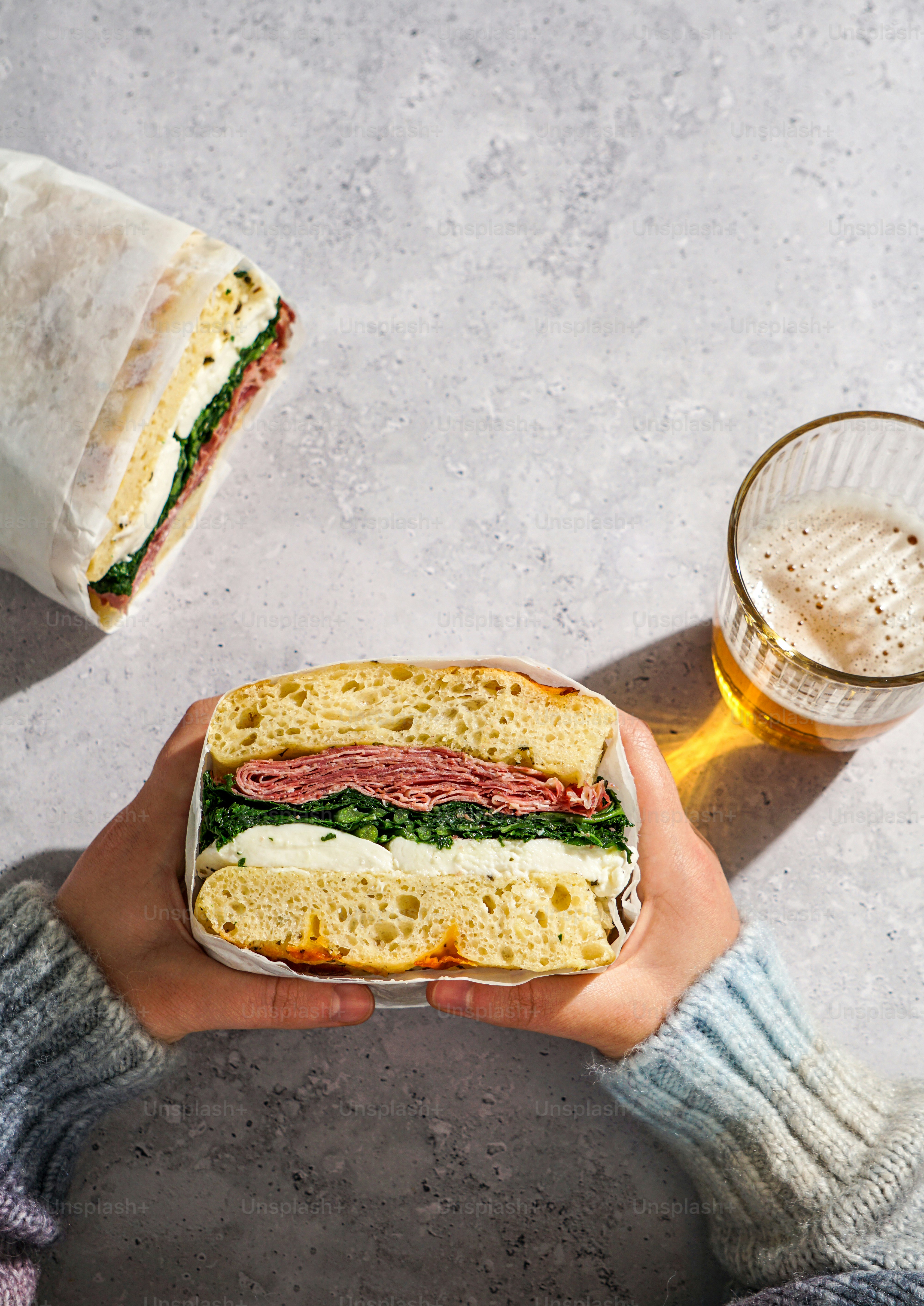 A person holding a sandwich and a glass of beer