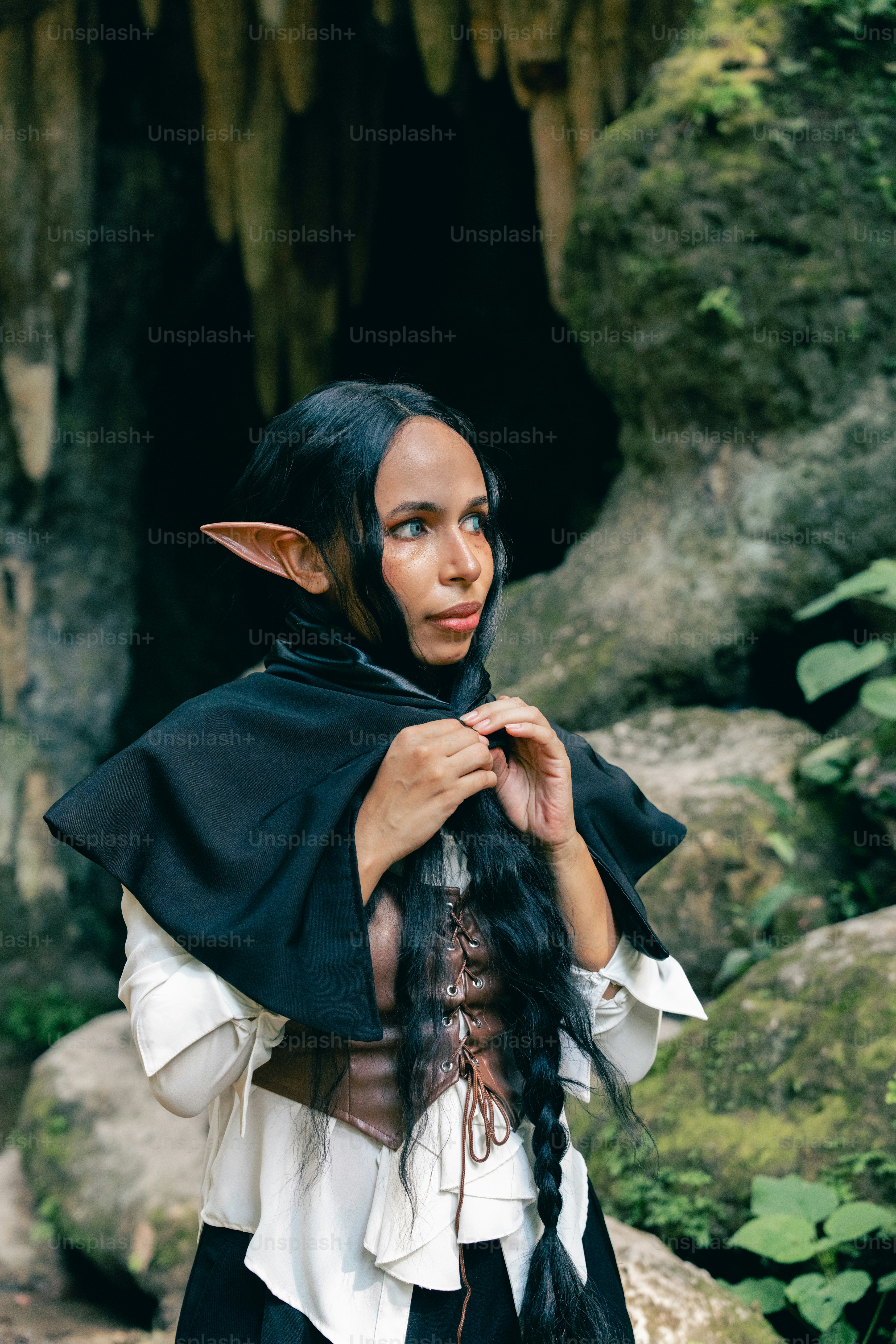 Una donna con un mantello nero in piedi davanti a una grotta