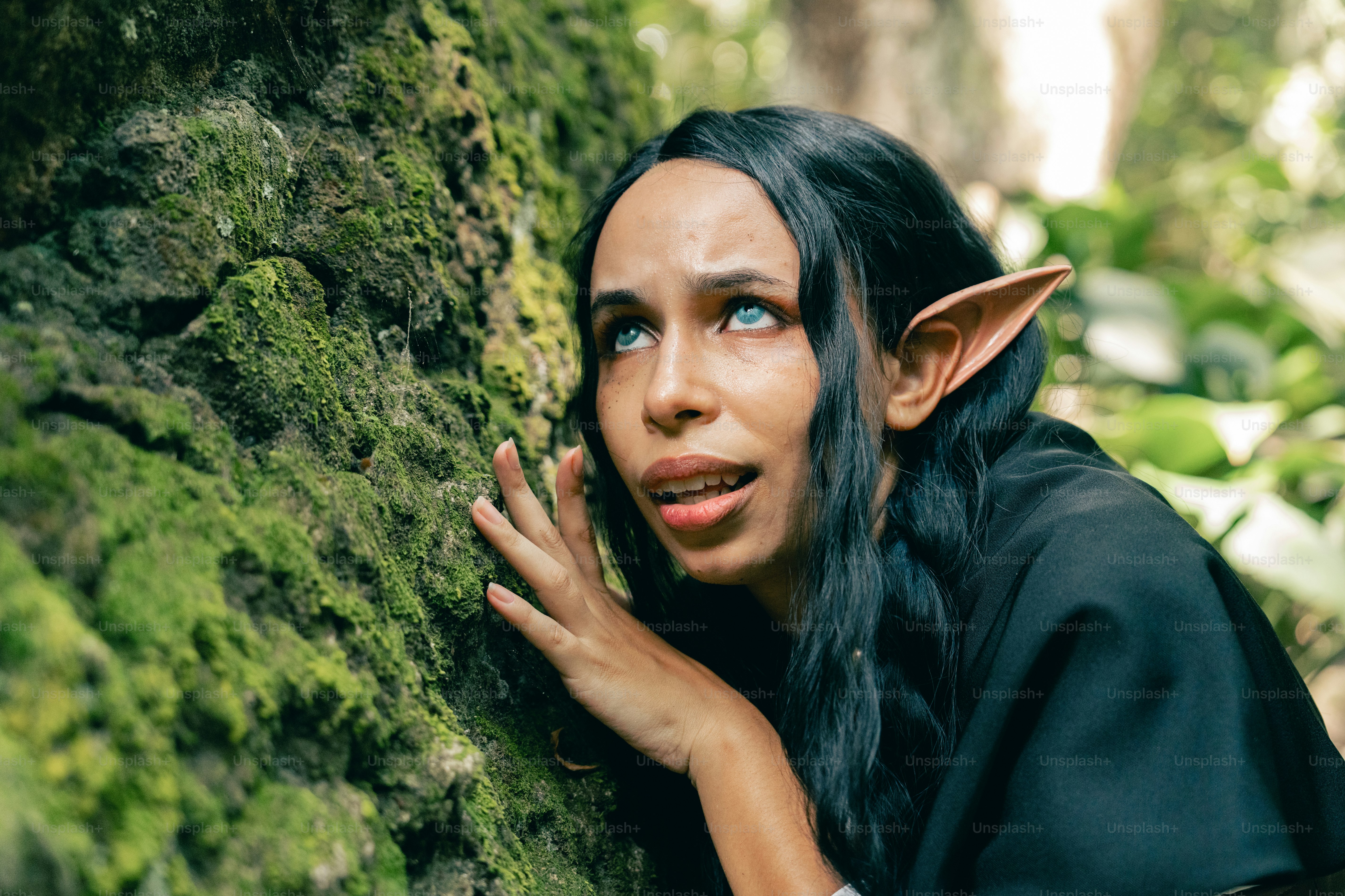 A woman with black hair leaning against a mossy tree