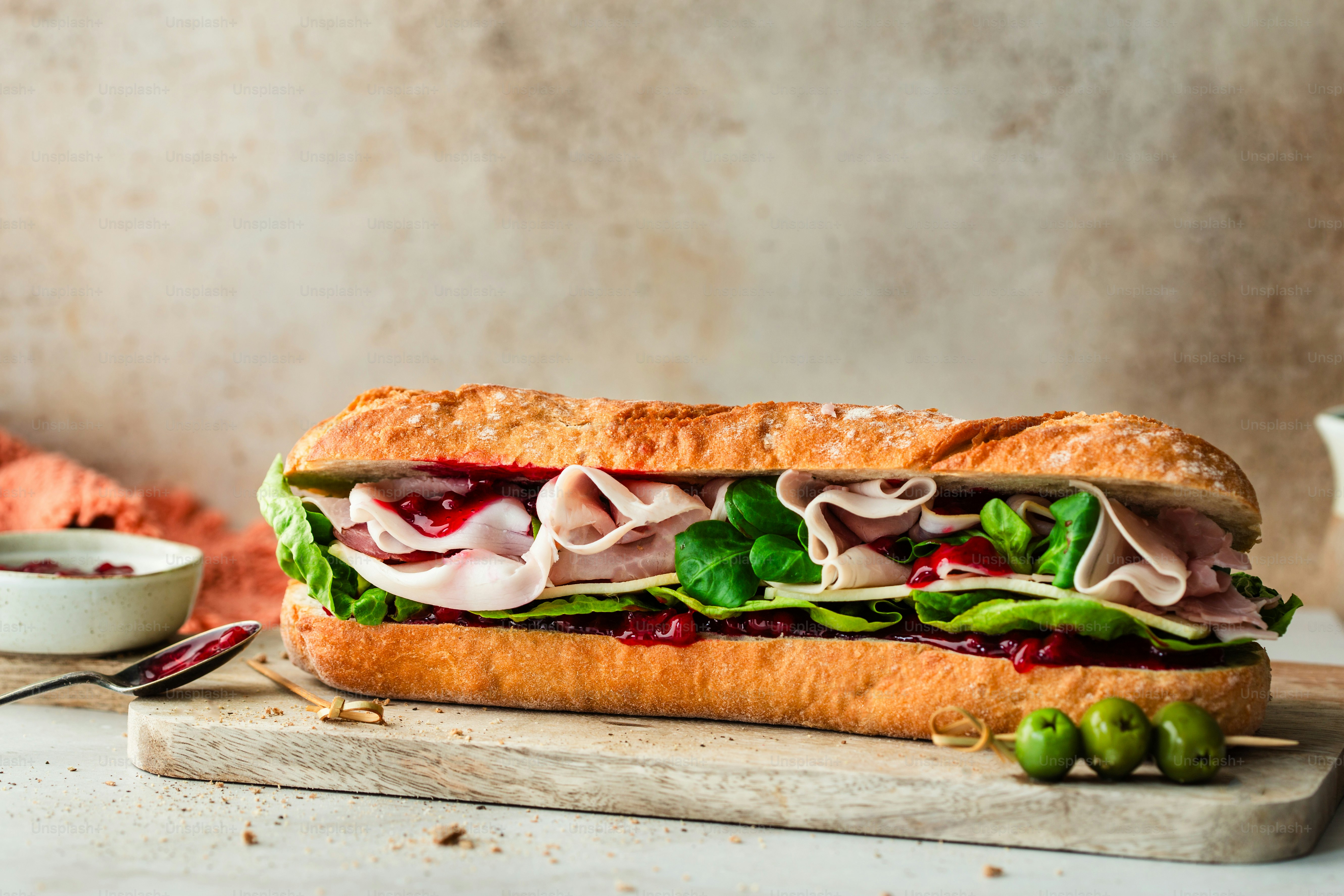A sub sandwich on a cutting board next to a bowl of soup