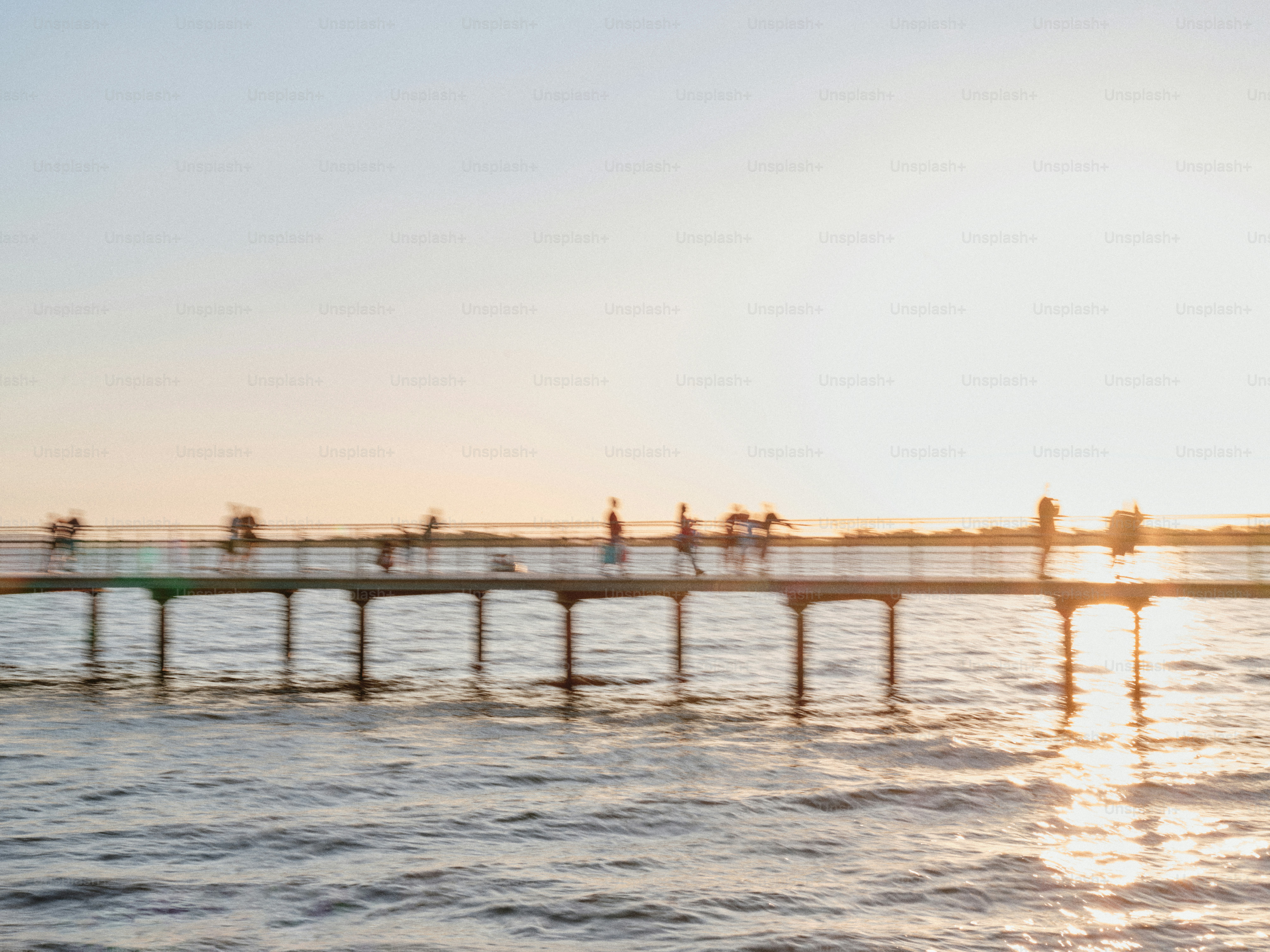 A group of people walking across a bridge over water photo – Blur Image ...
