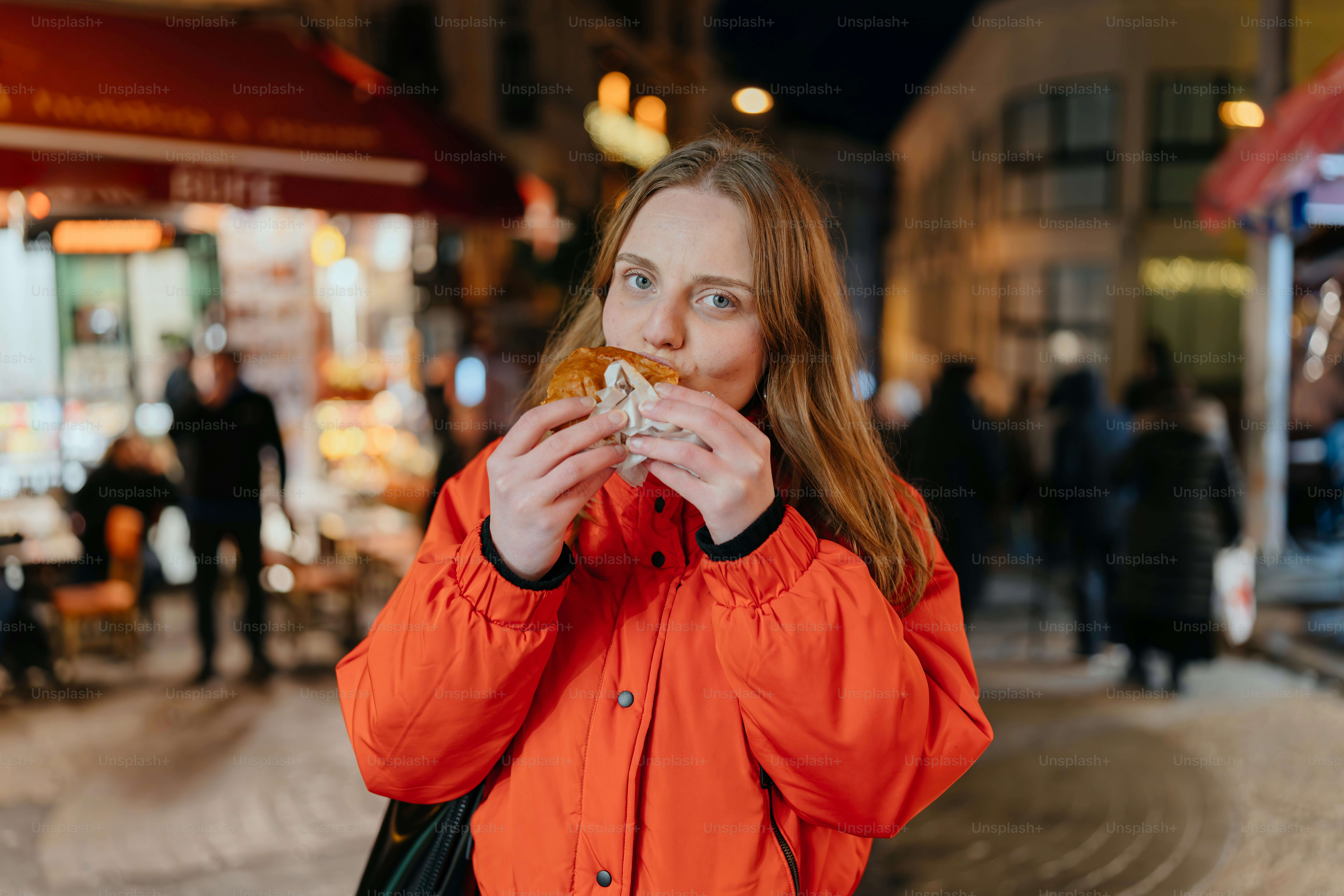 A woman in an orange jacket eating a doughnut