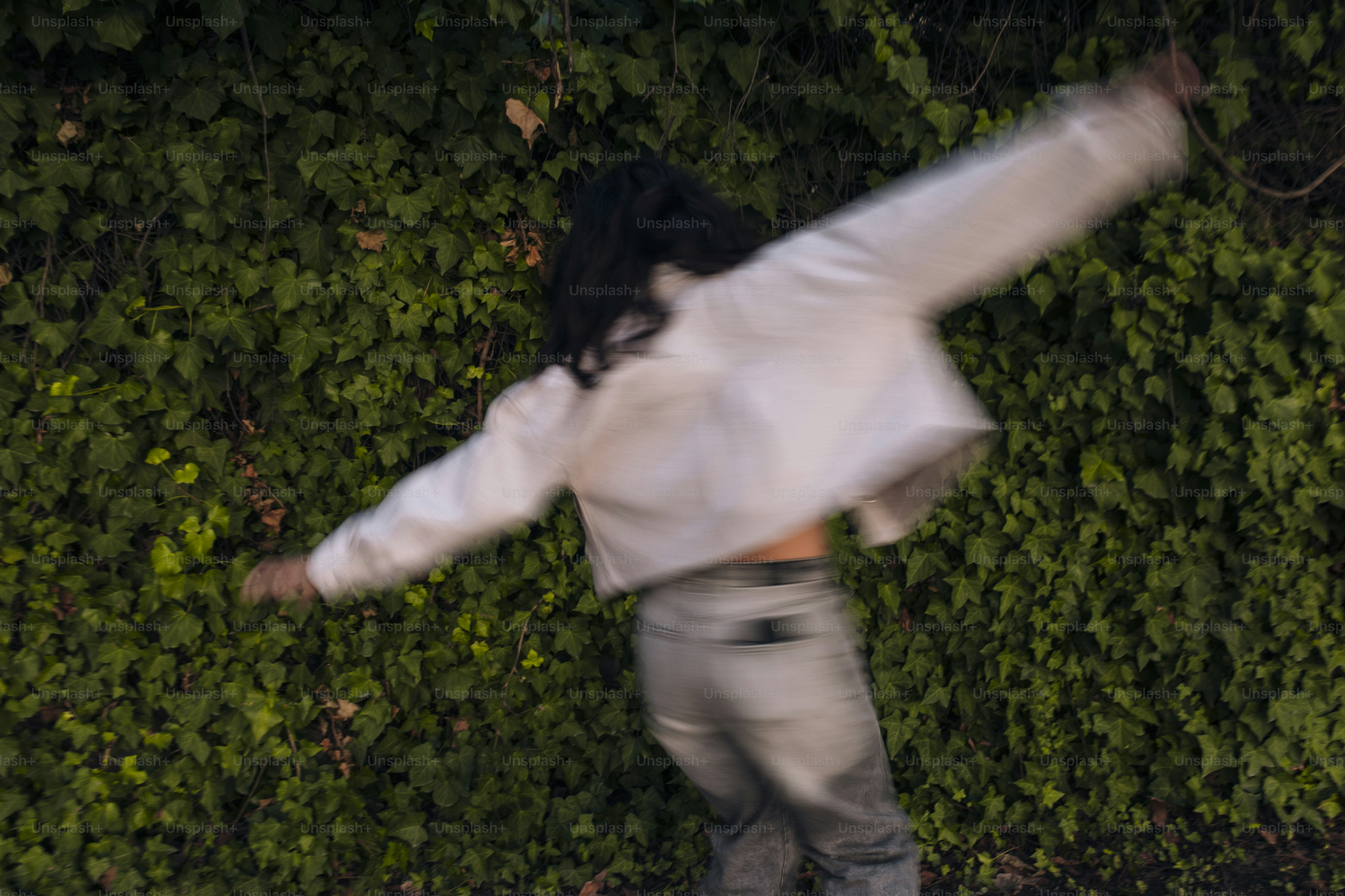 A man riding a skateboard down a street next to a lush green wall