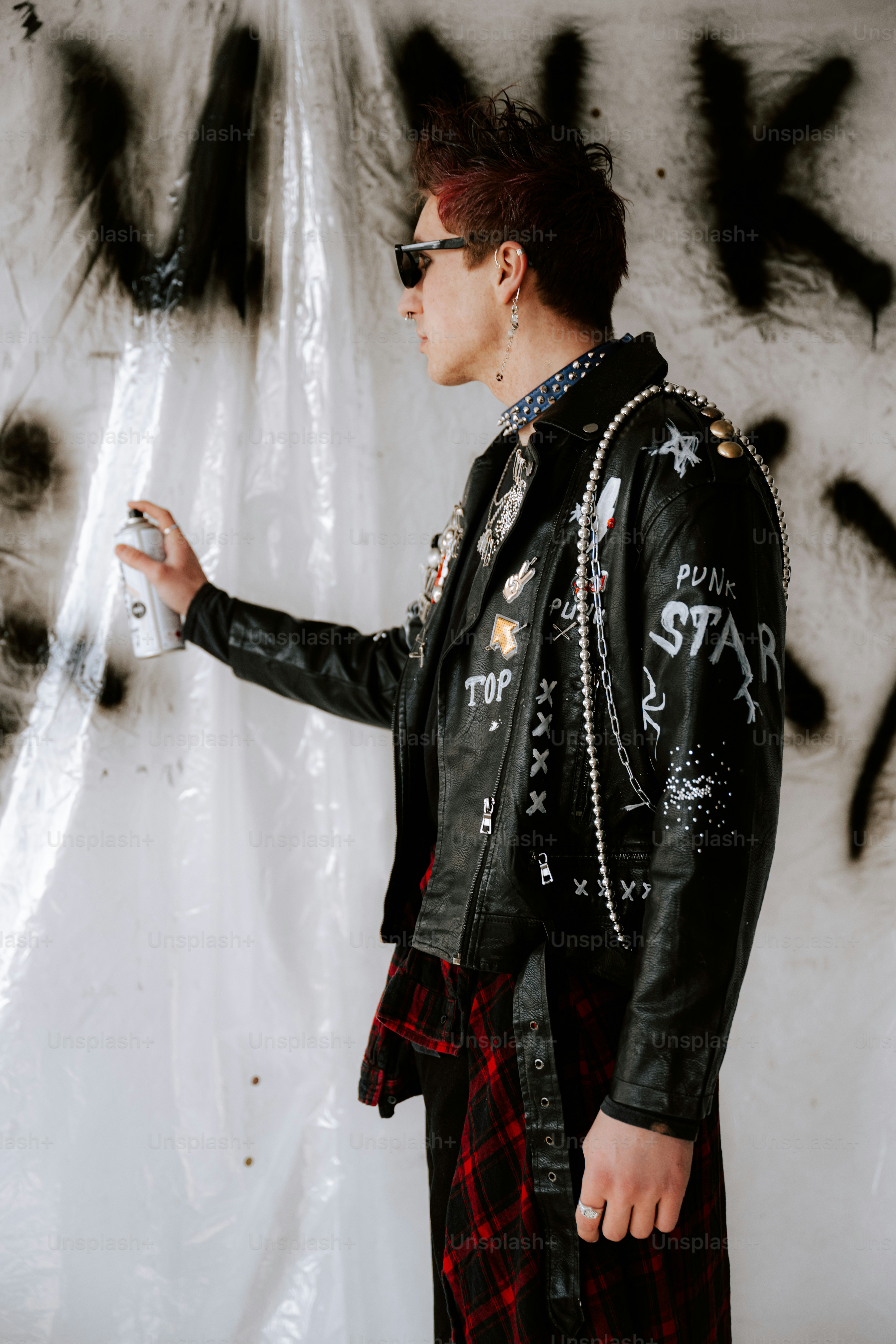 A man in a black leather jacket standing in front of a graffiti covered wall