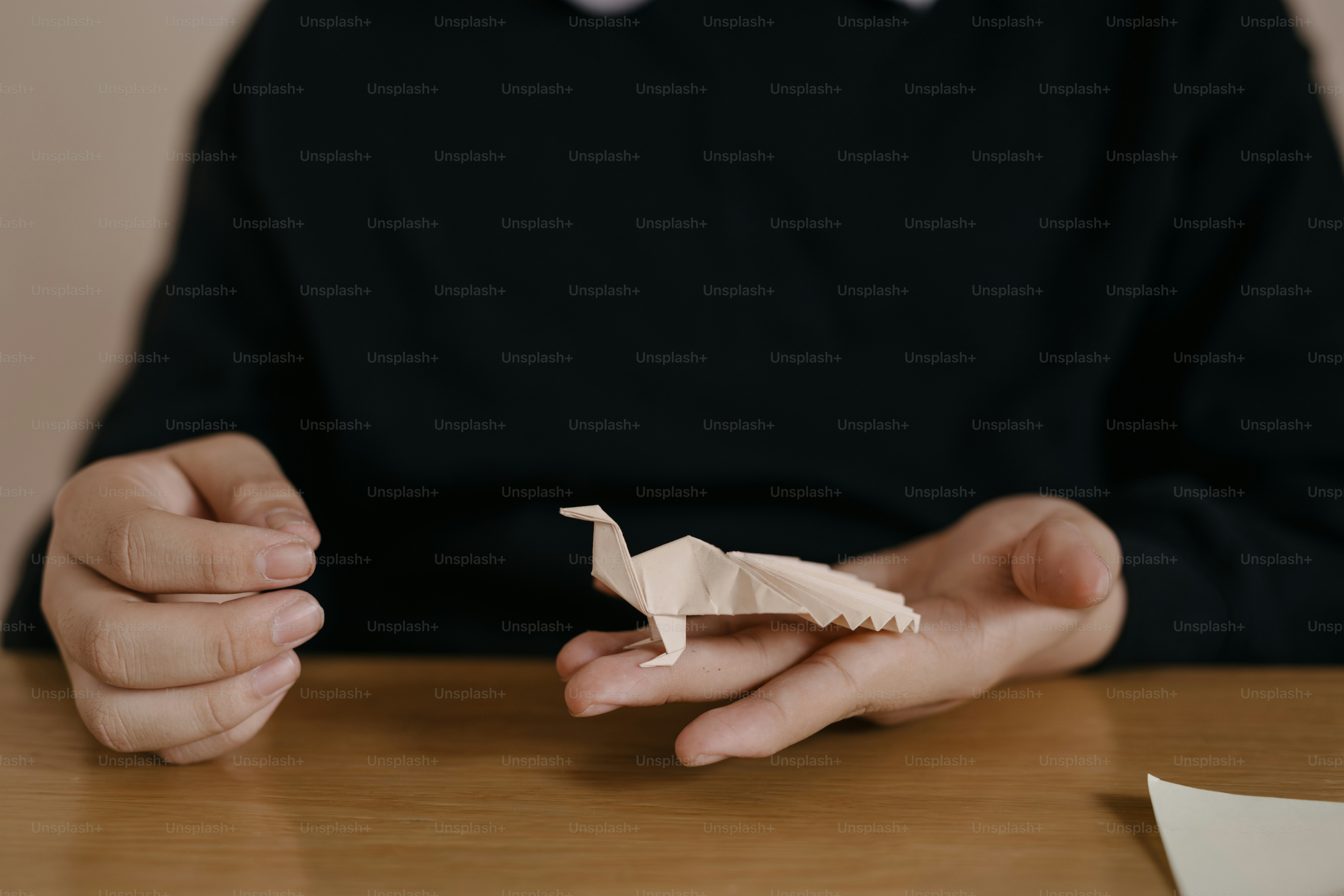 Eine Person, die mit einem Papiervogel in den Händen an einem Tisch sitzt