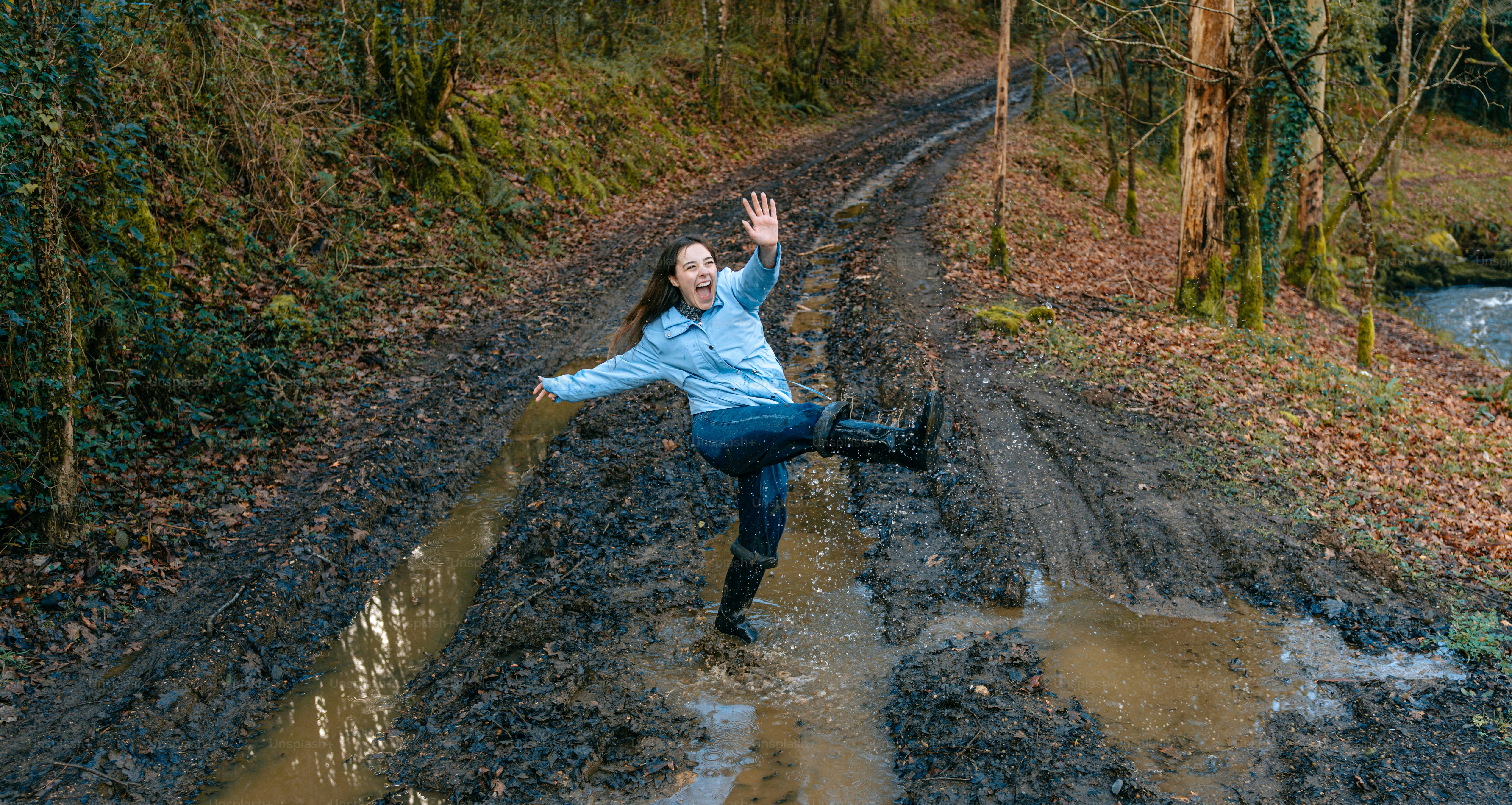 A woman in a blue jacket is jumping in the mud
