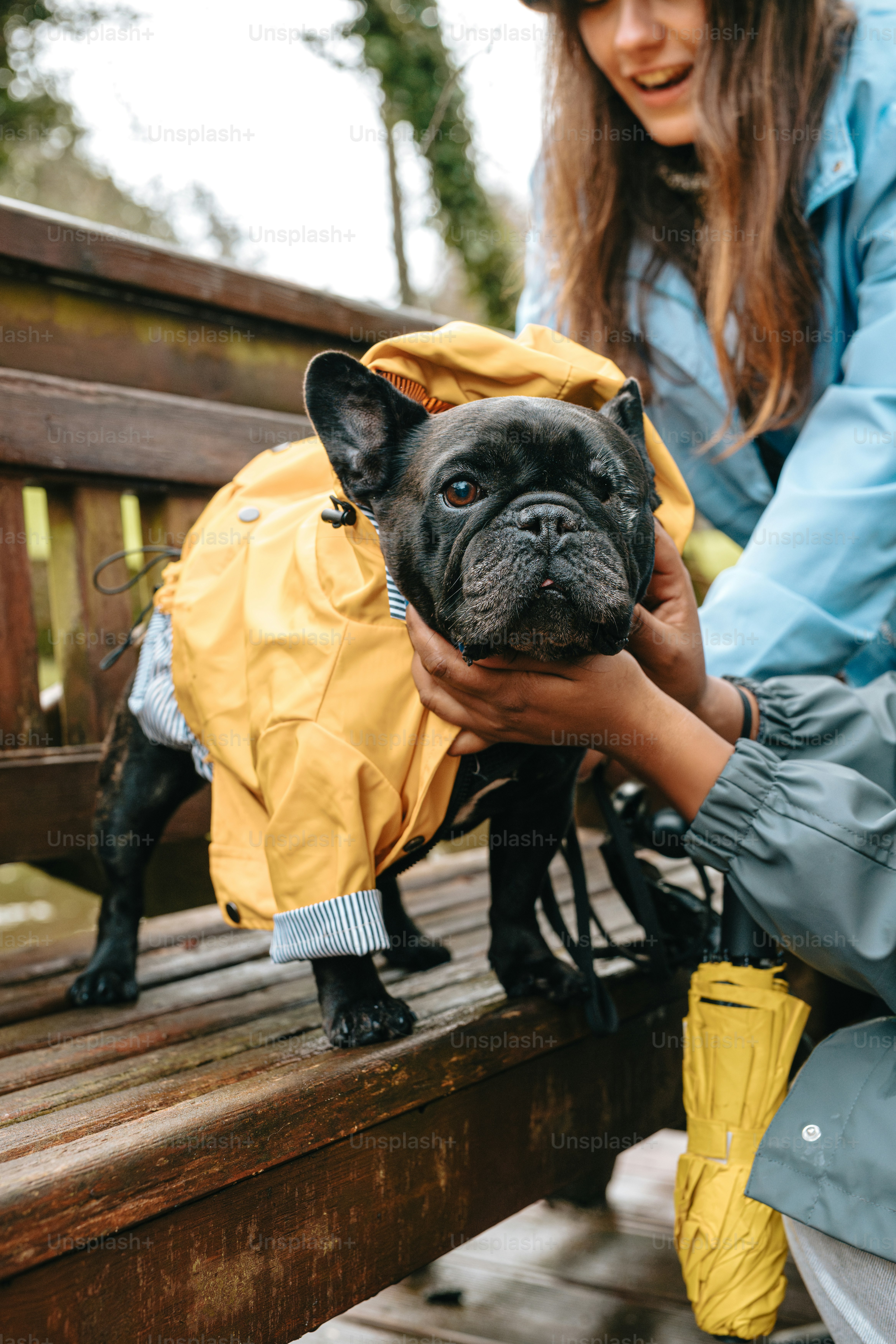 A woman petting a dog wearing a raincoat