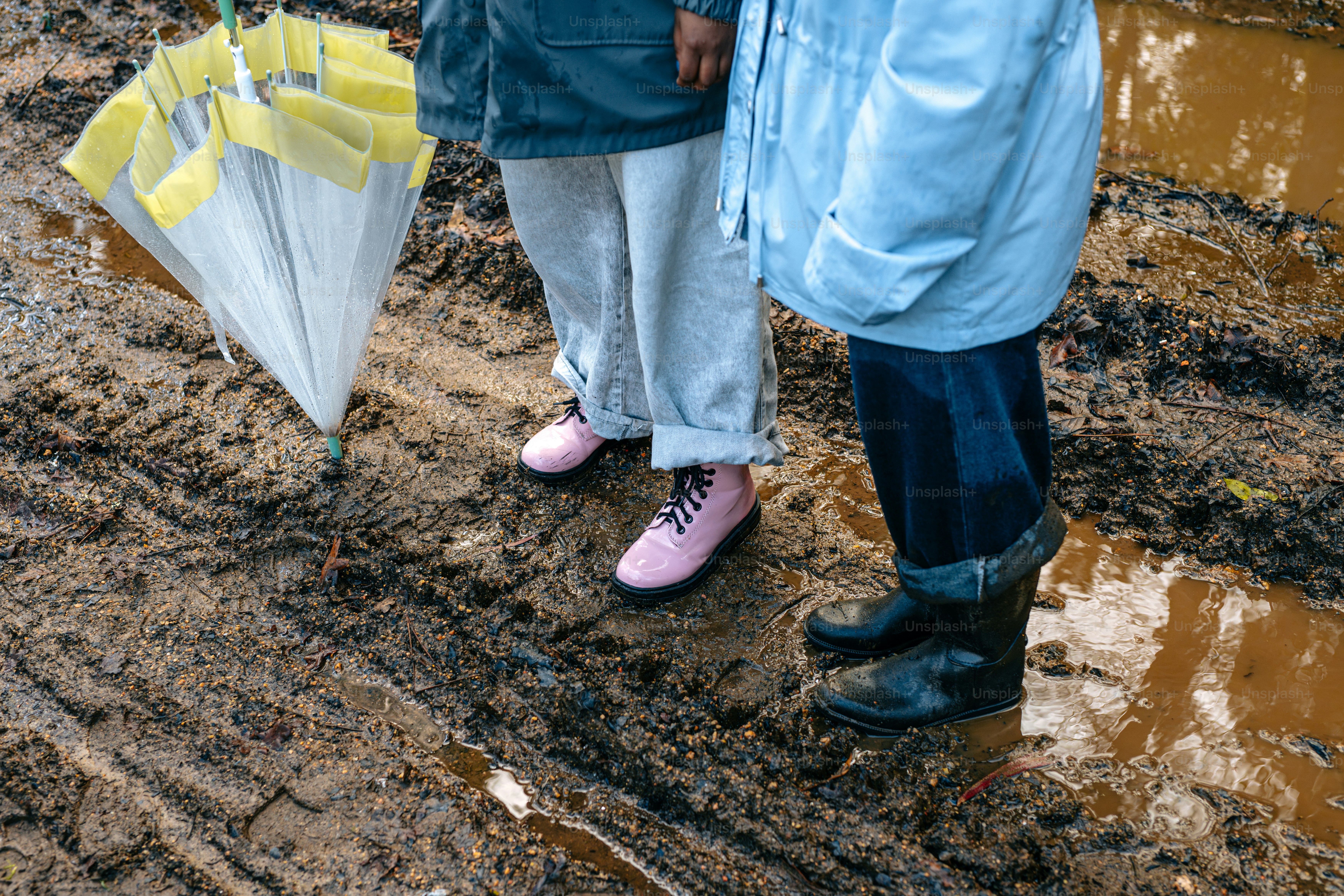 Two people standing in the mud holding umbrellas