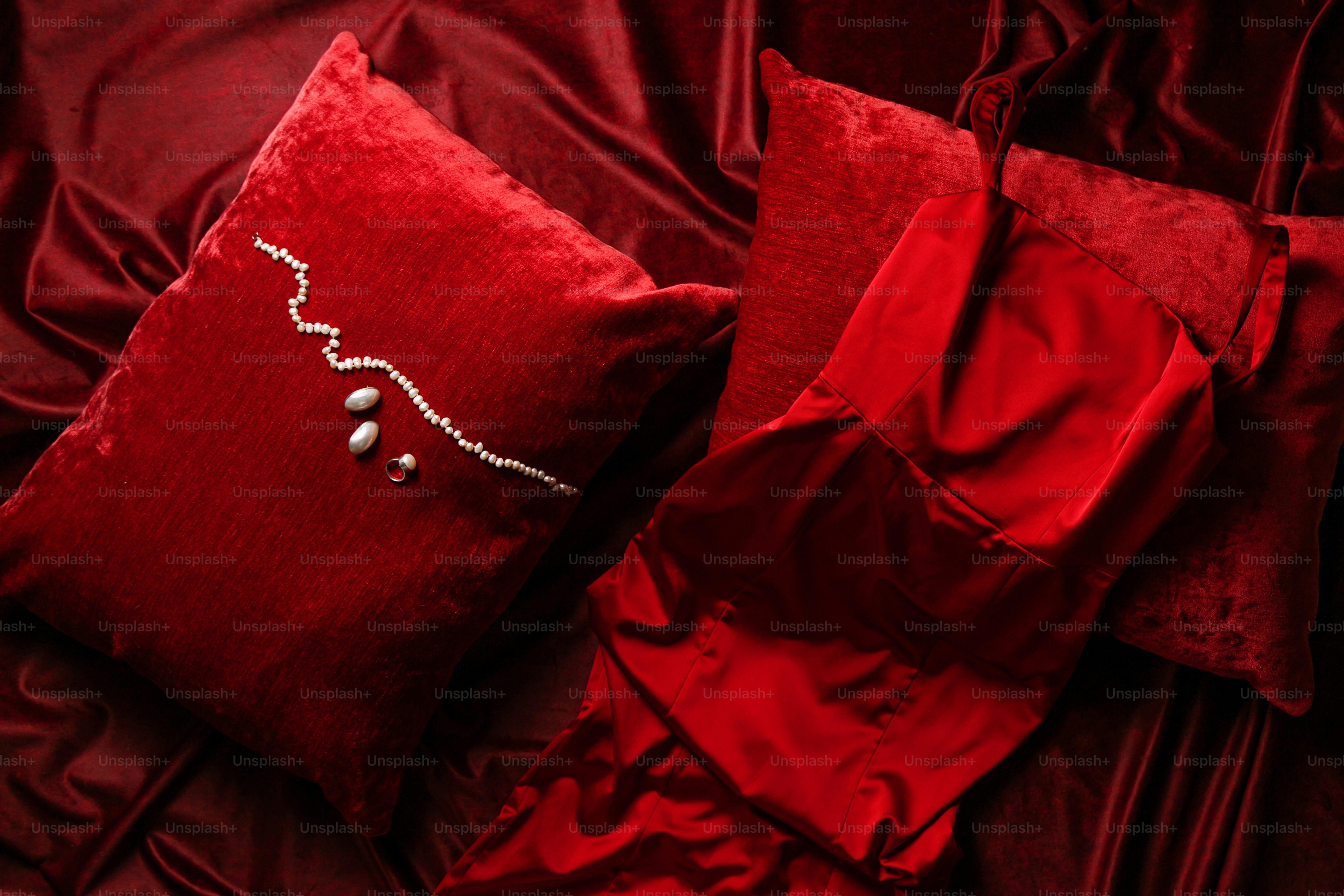 A red pillow and some red sheets on a bed