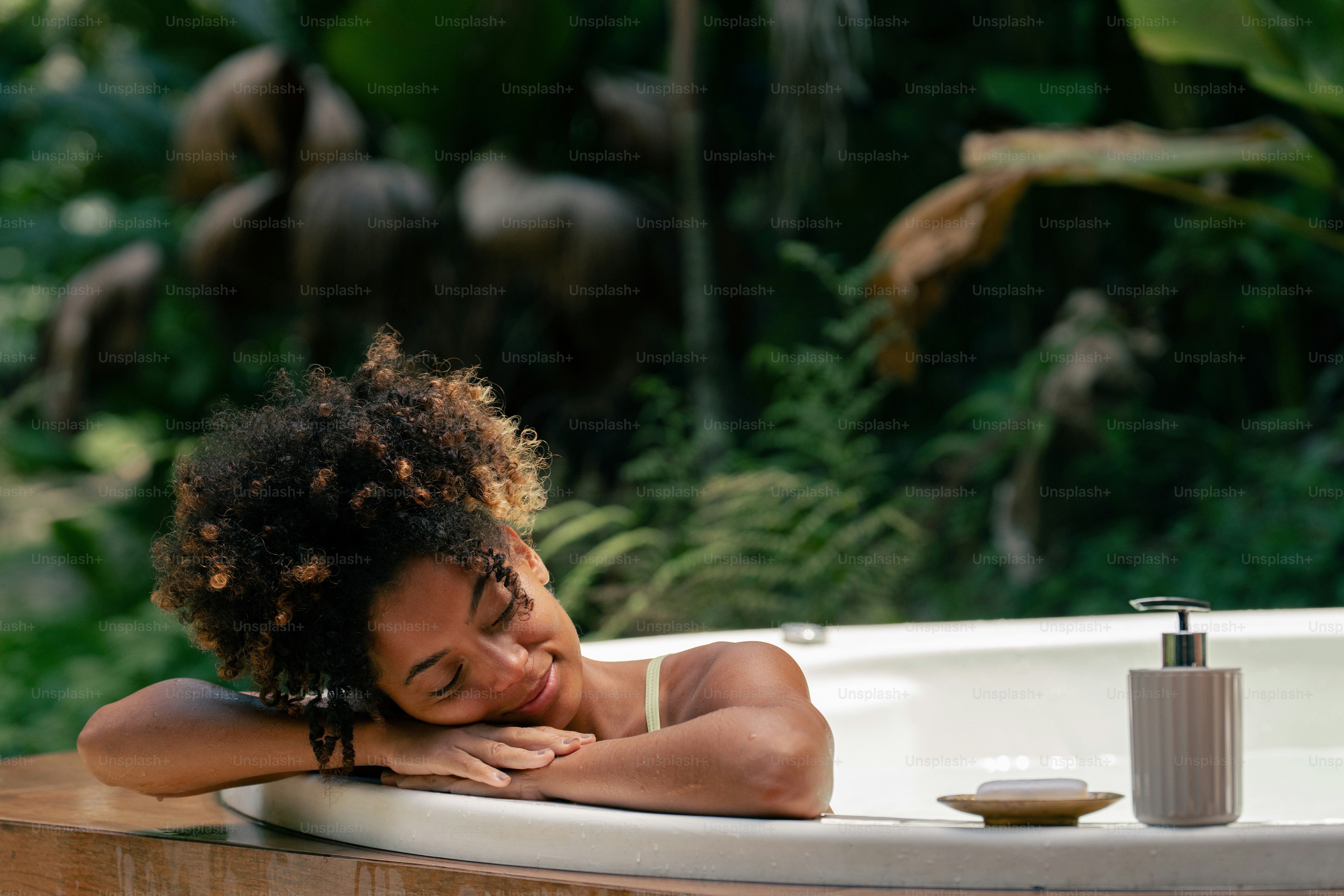 Woman resting in an outdoor bathtub surrounded by greenery