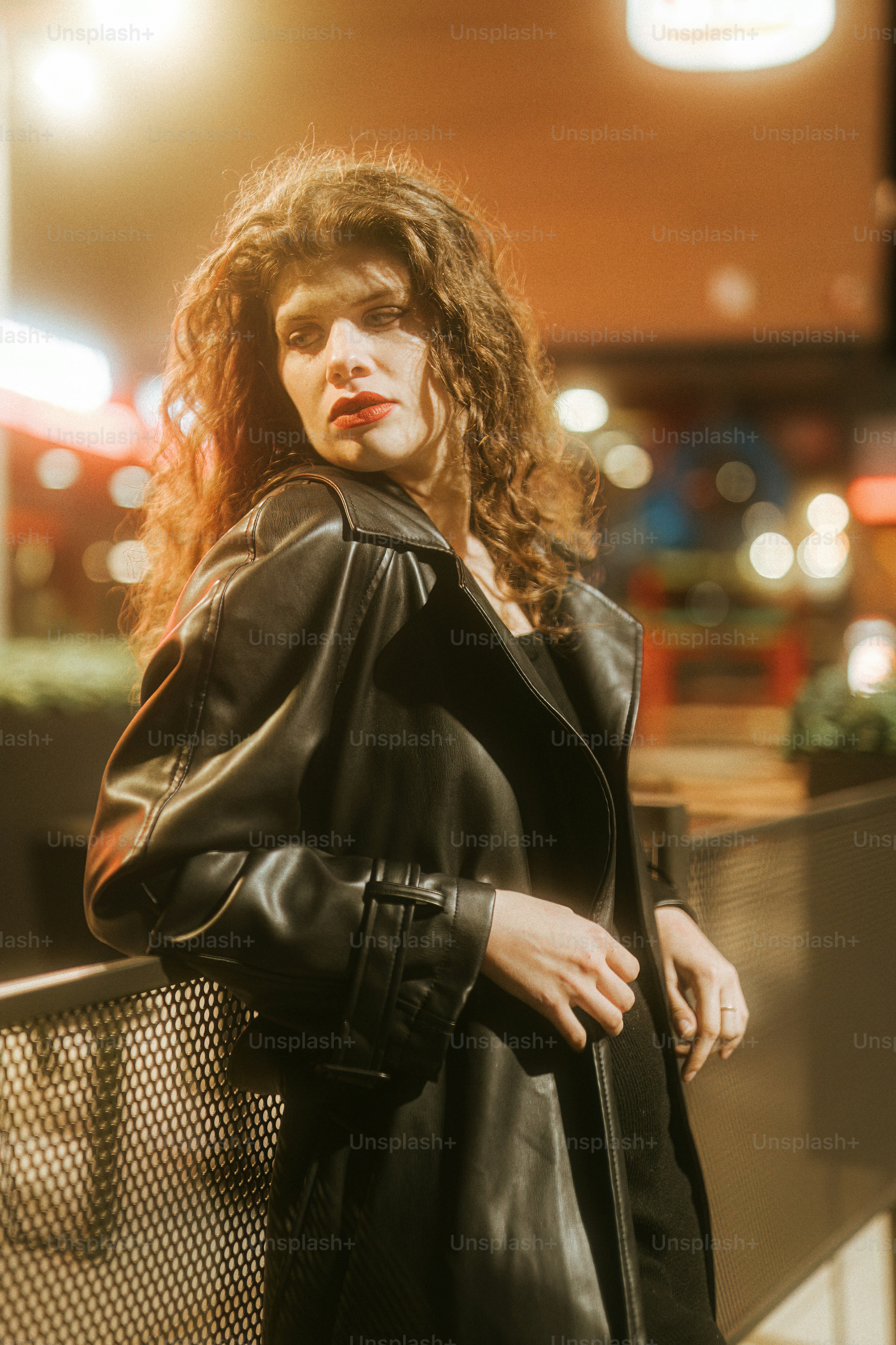 A woman in a black leather jacket leaning against a fence