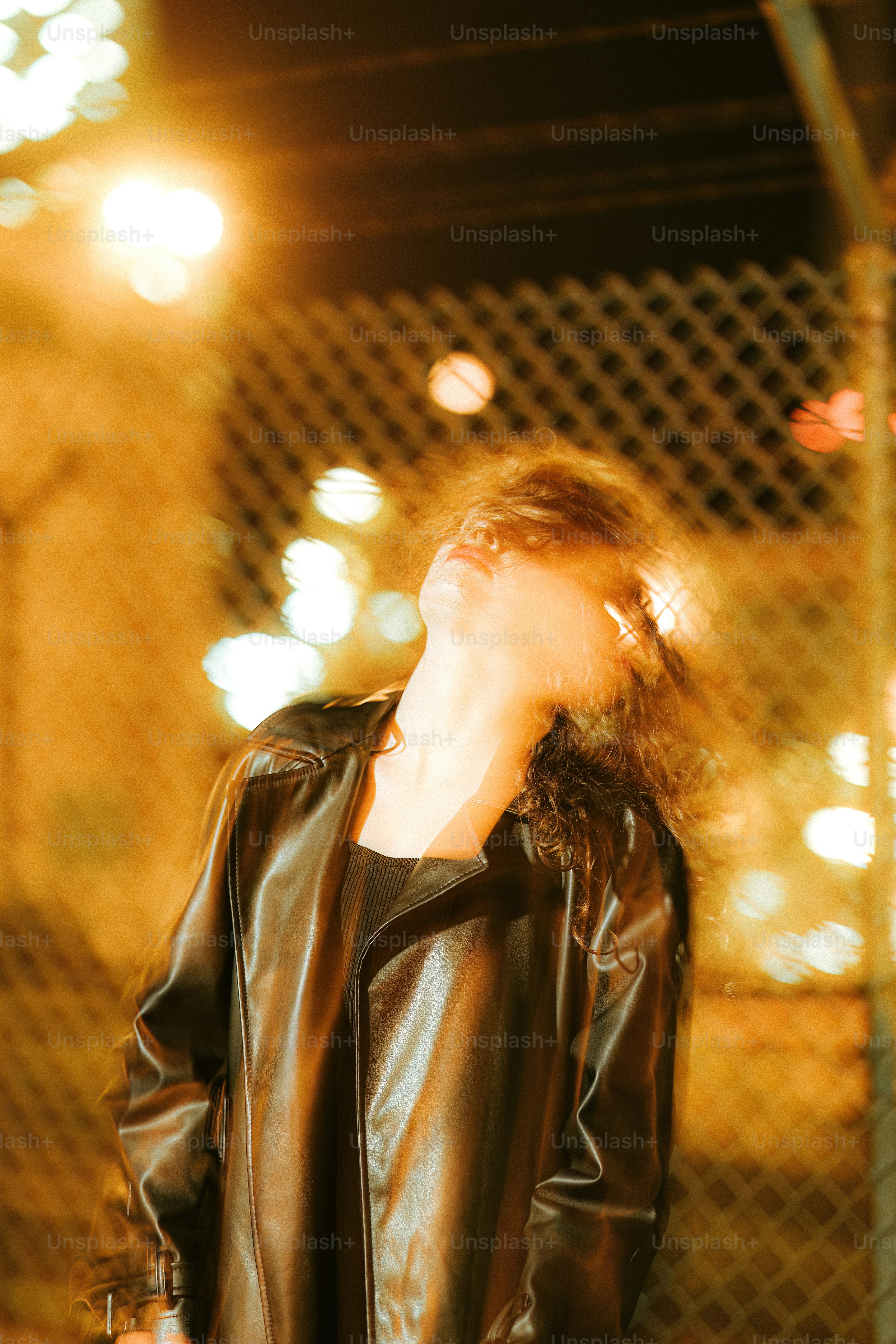 A woman in a black leather jacket standing in front of a fence photo ...