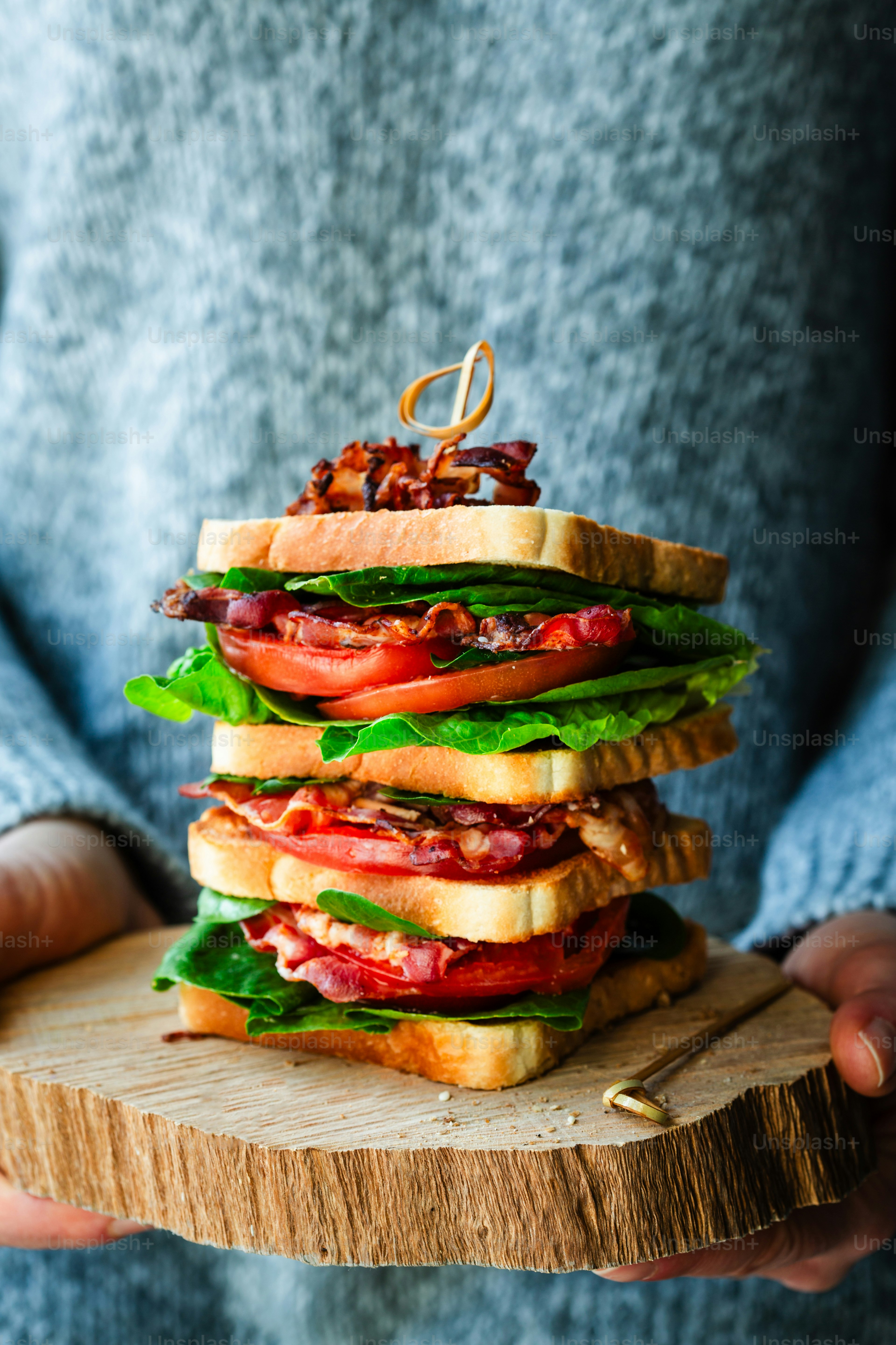 A person holding a wooden board with a sandwich on it