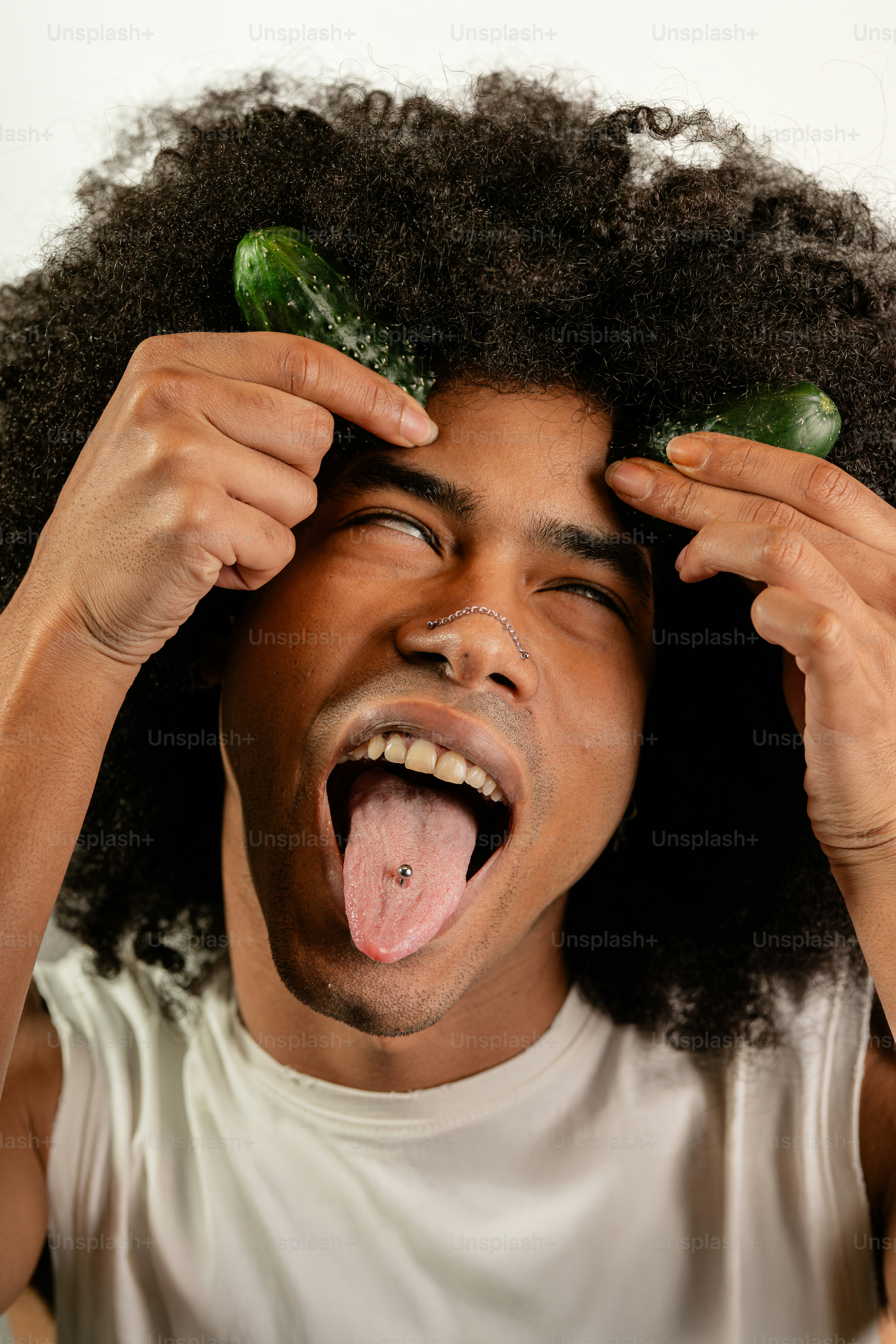 A young man is holding cucumbers in his hair