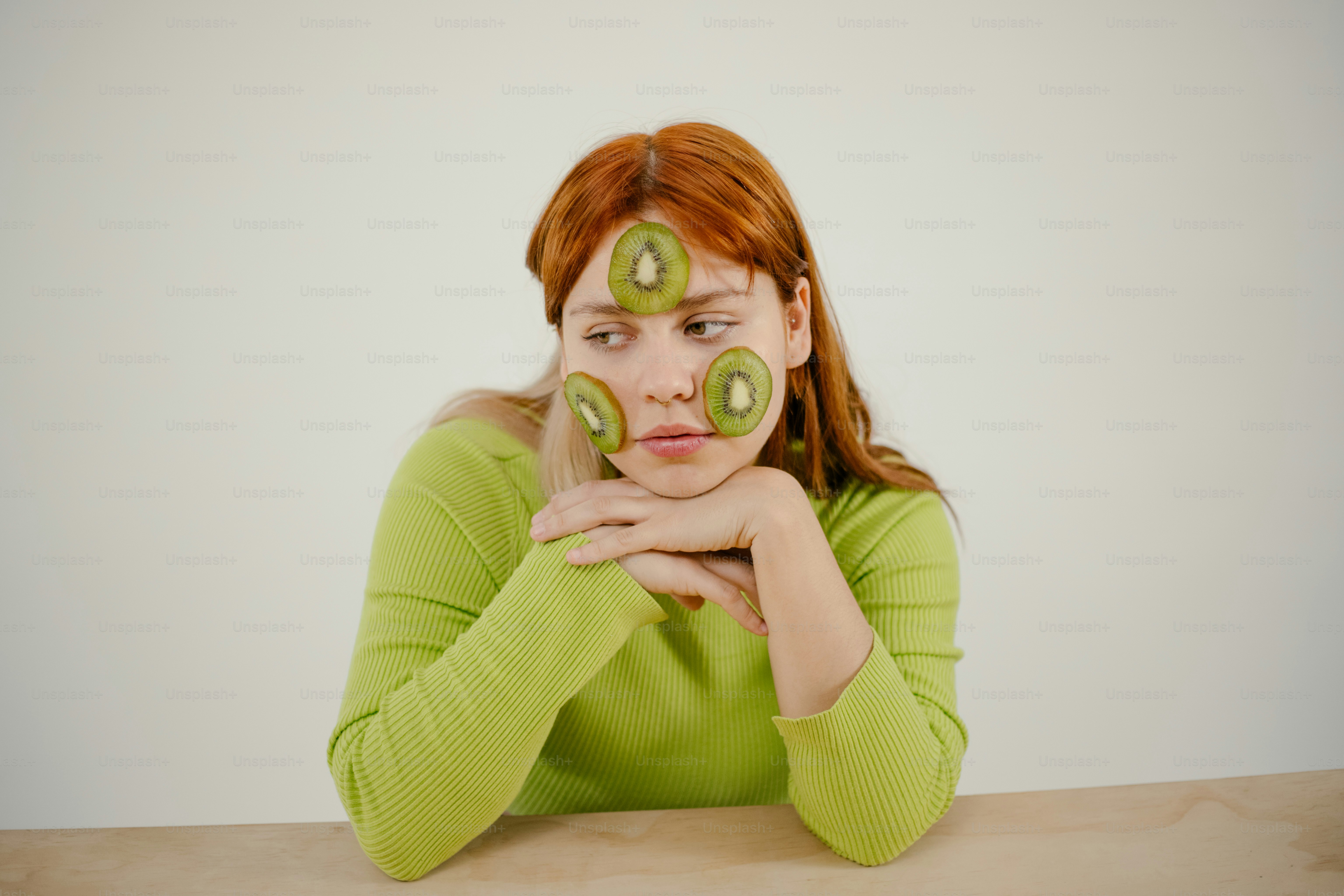 테이블에 앉아 아보카도 두 조각을 얼굴에 바르고 있는 여성