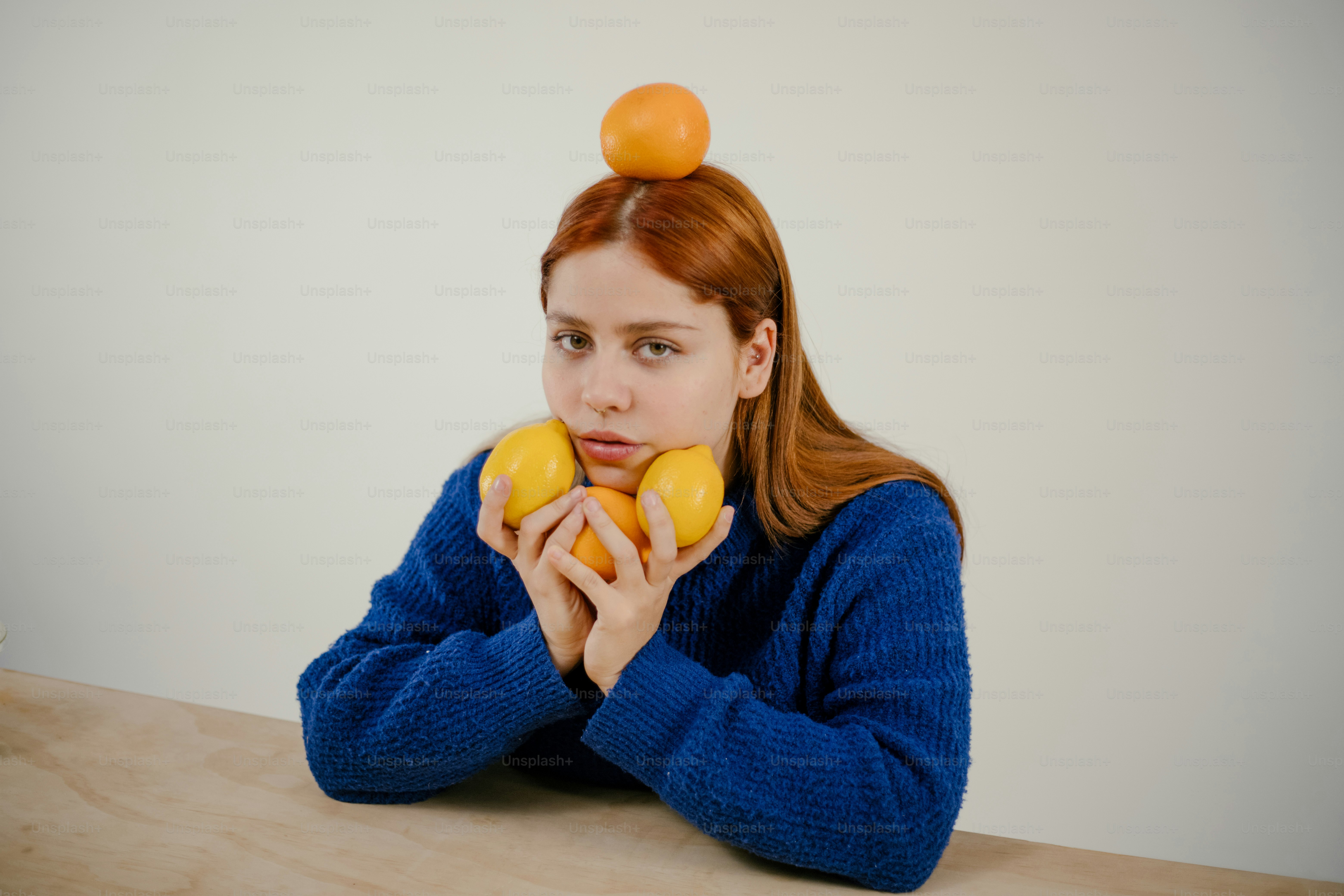 A woman sitting at a table with oranges on her head