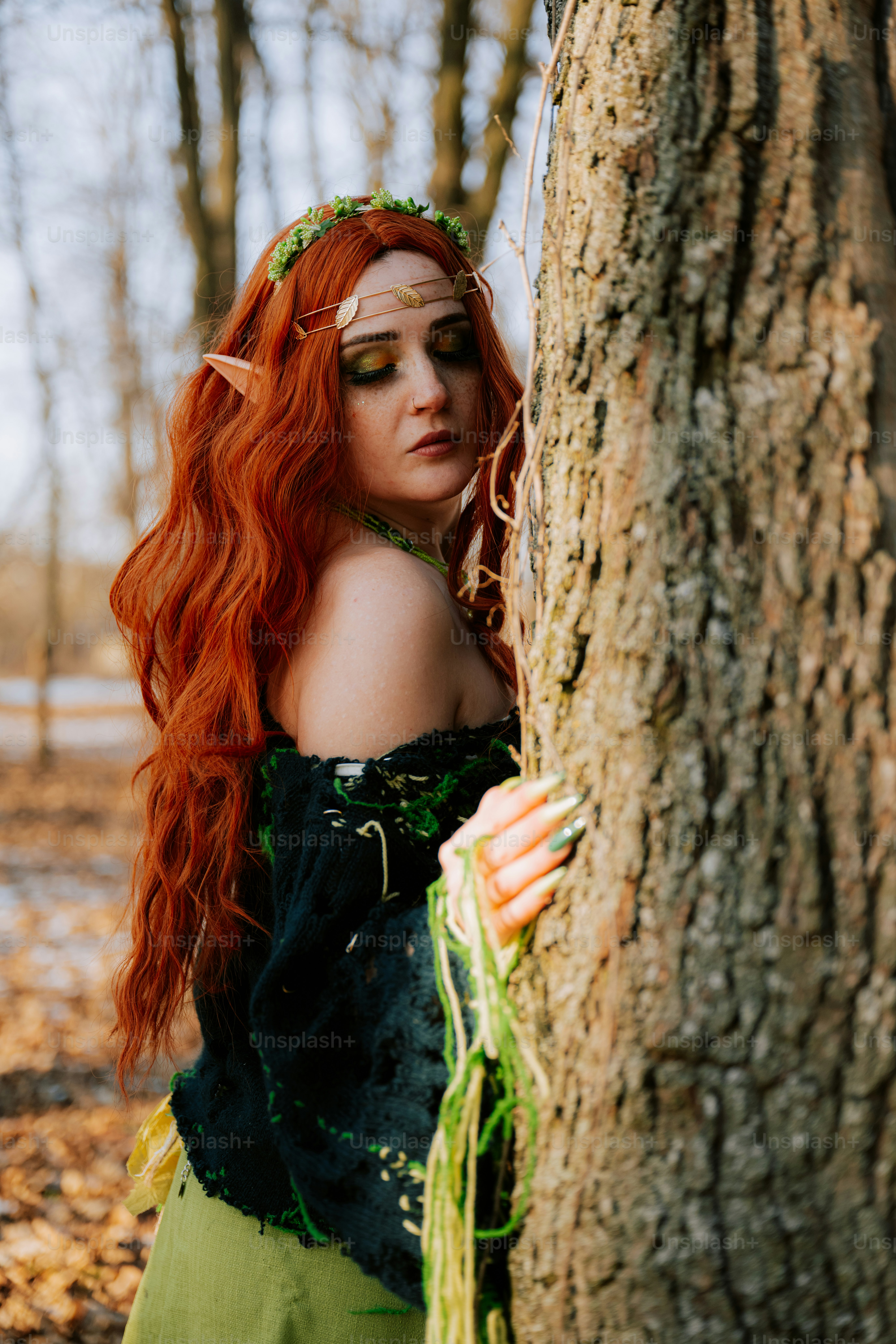 Une femme aux longs cheveux roux debout à côté d’un arbre
