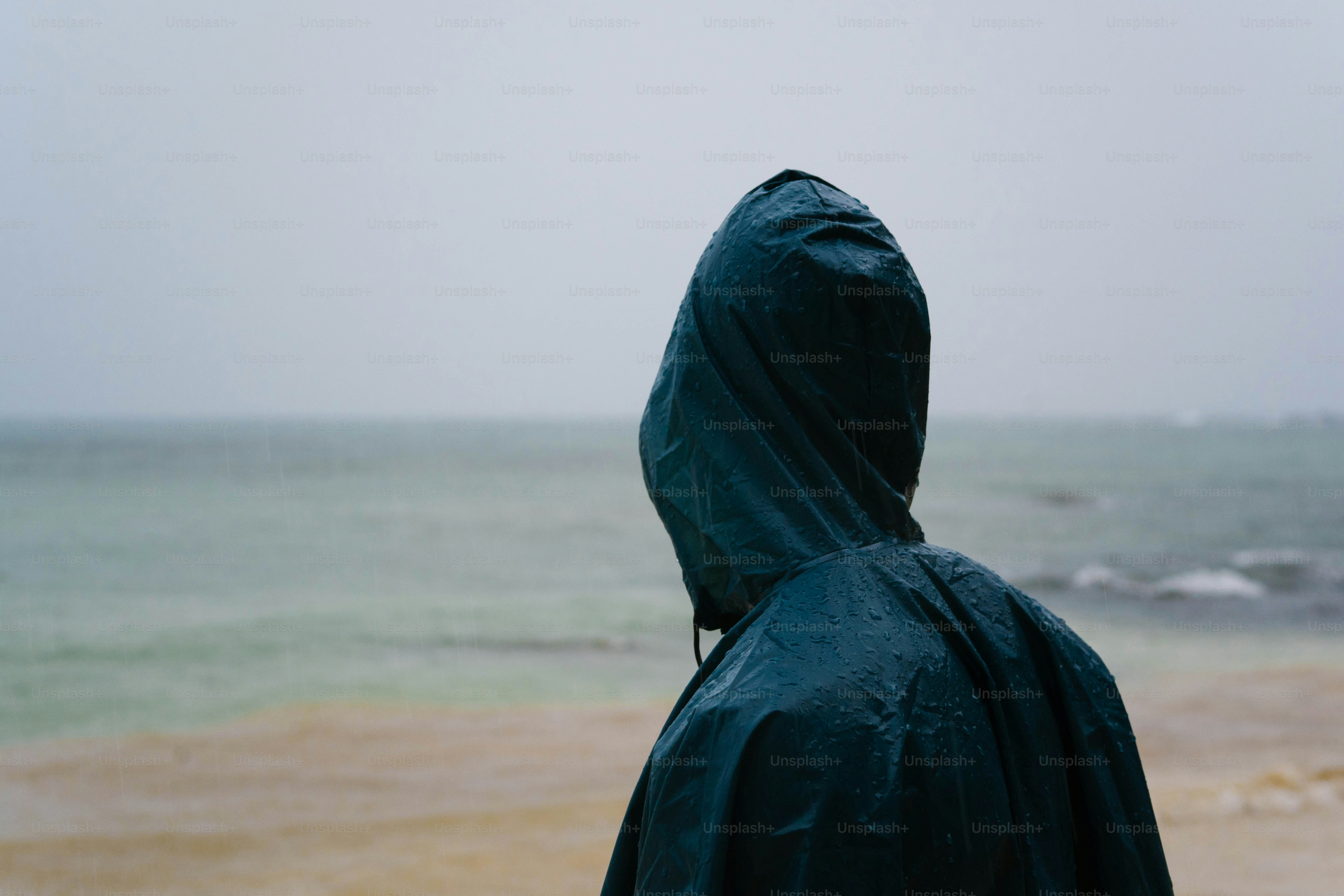 A person in a hooded jacket looking out at the ocean