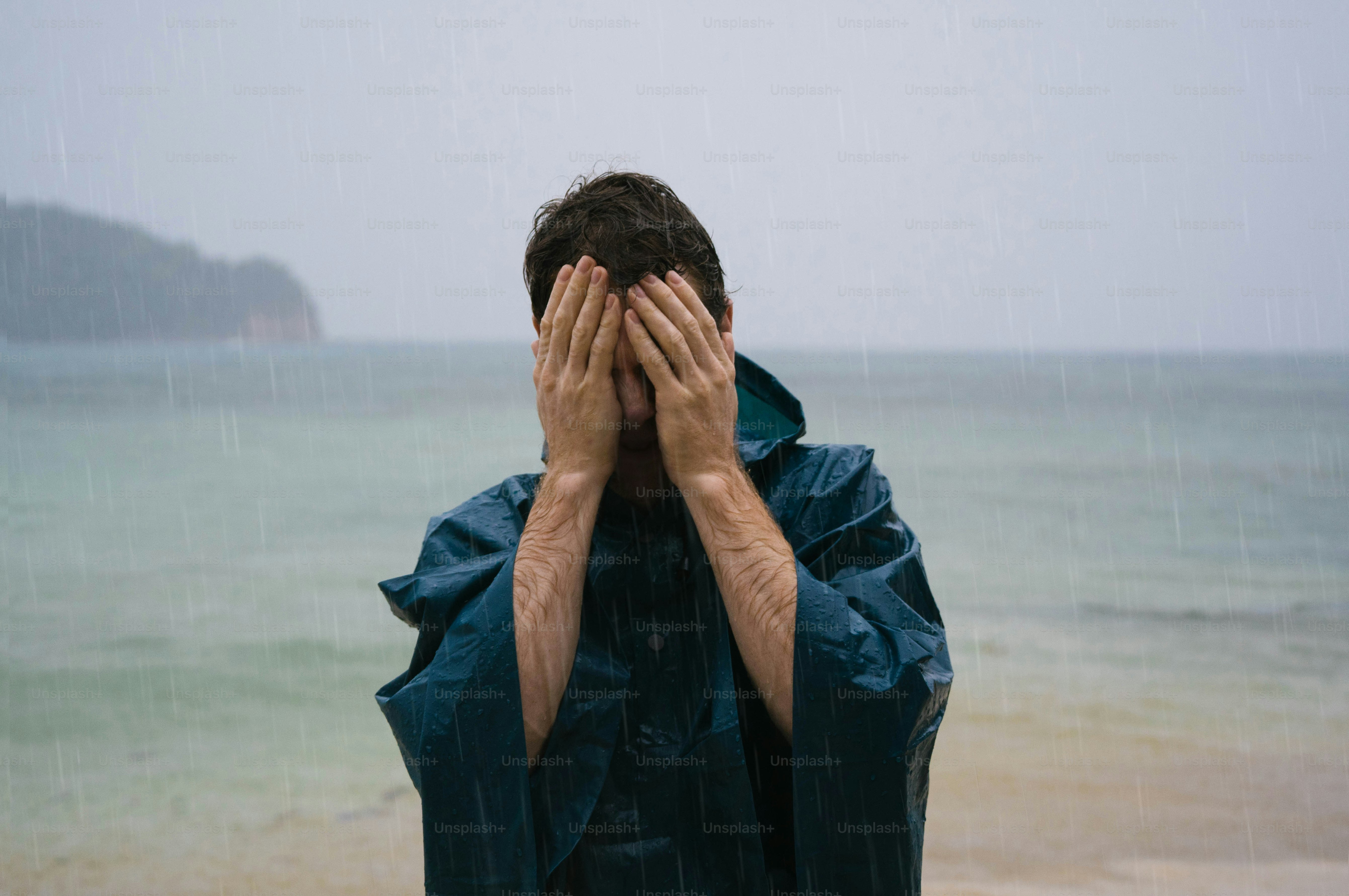 A man covers his face while standing on a beach