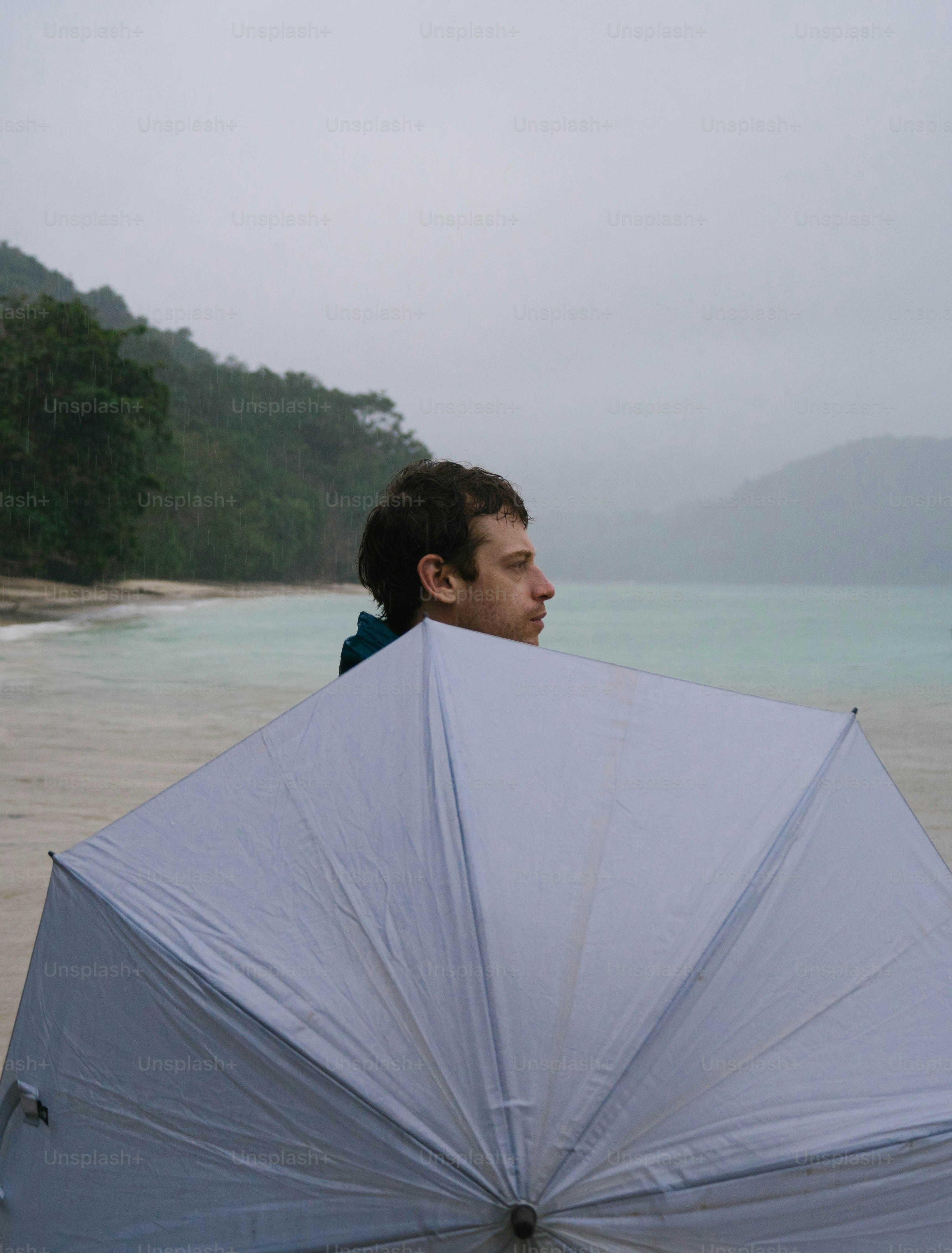 Ein Mann, der an einem Strand steht und einen Sonnenschirm in der Hand hält