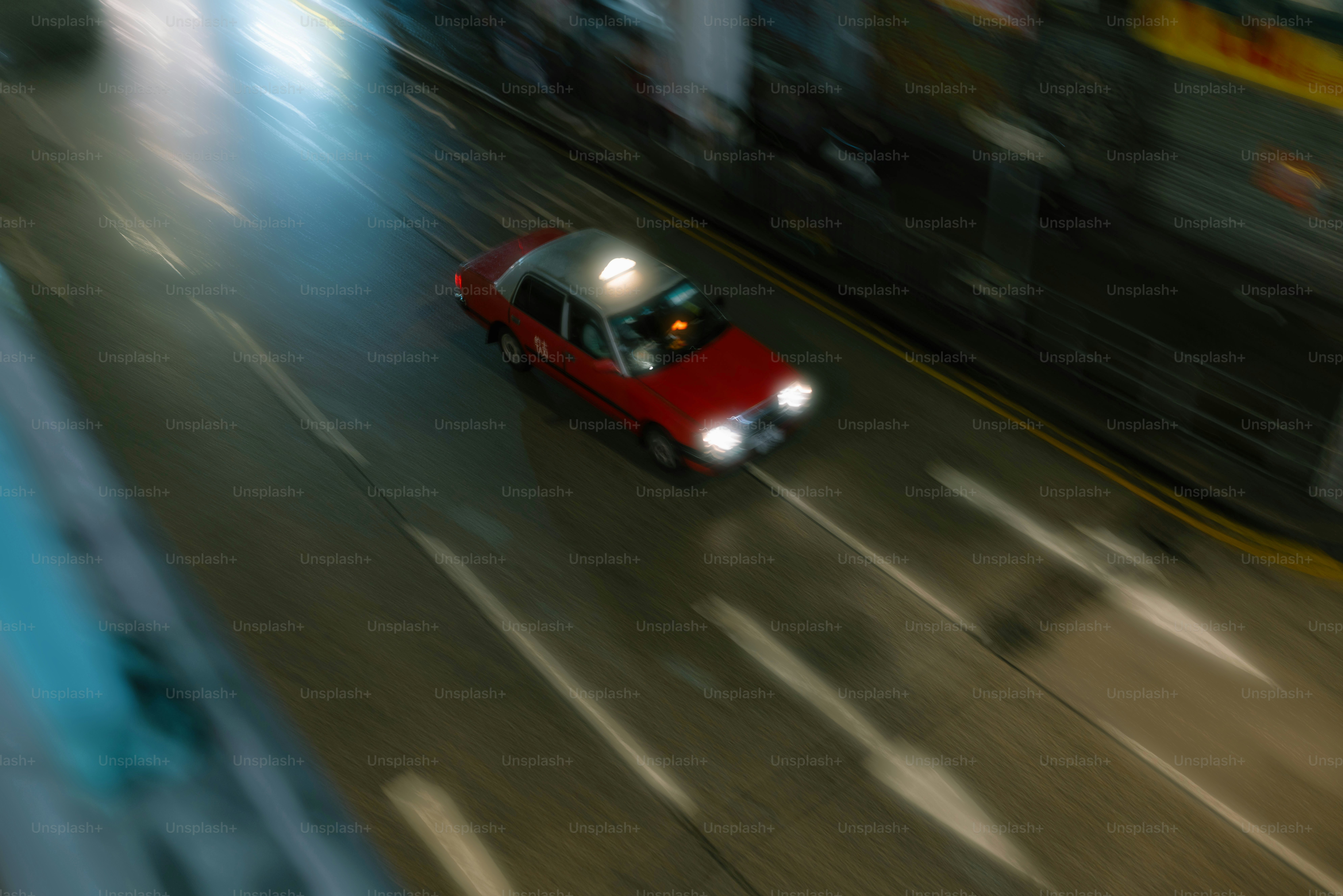 A red car driving down a street next to tall buildings