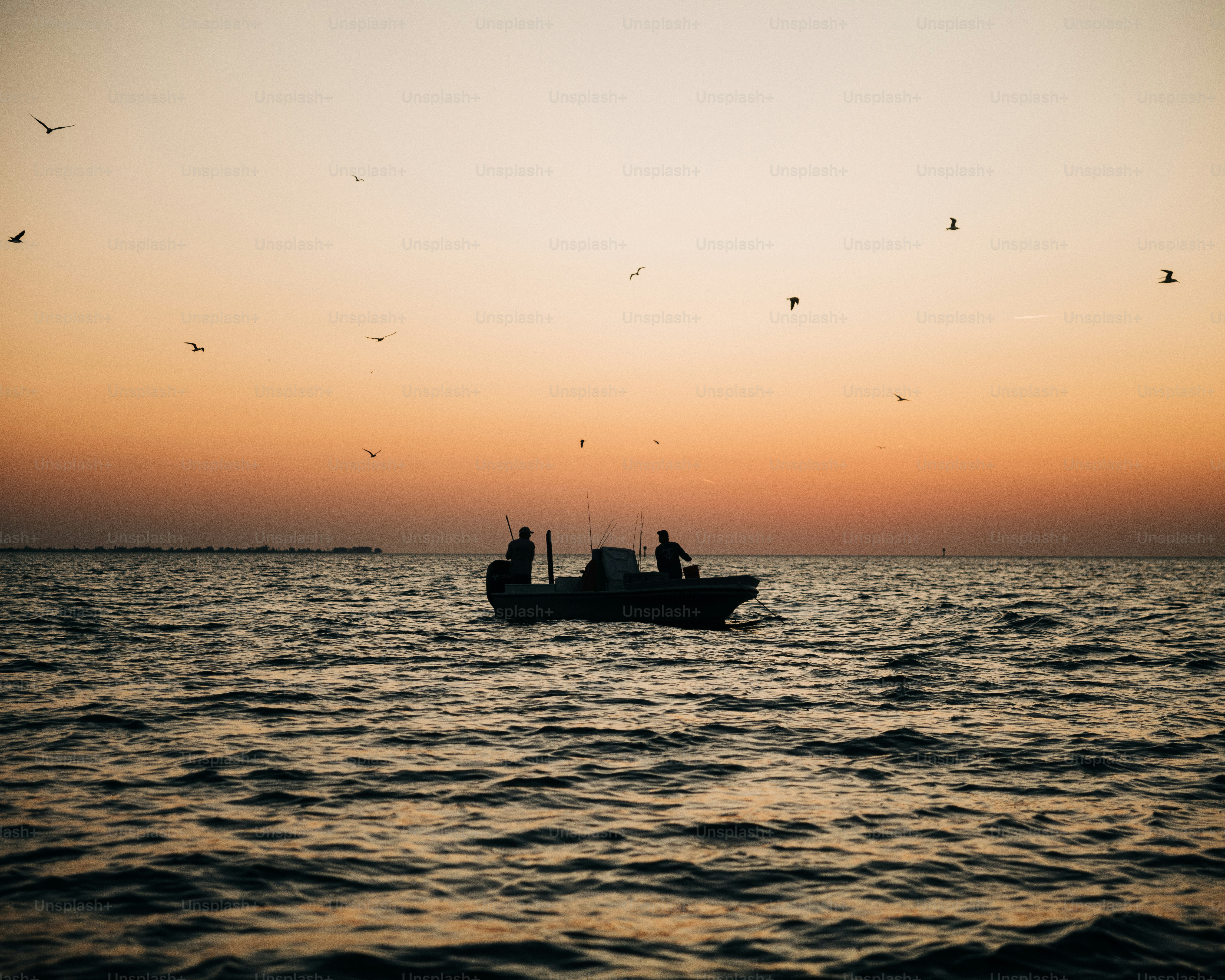 Two people fish from a boat at sunset.