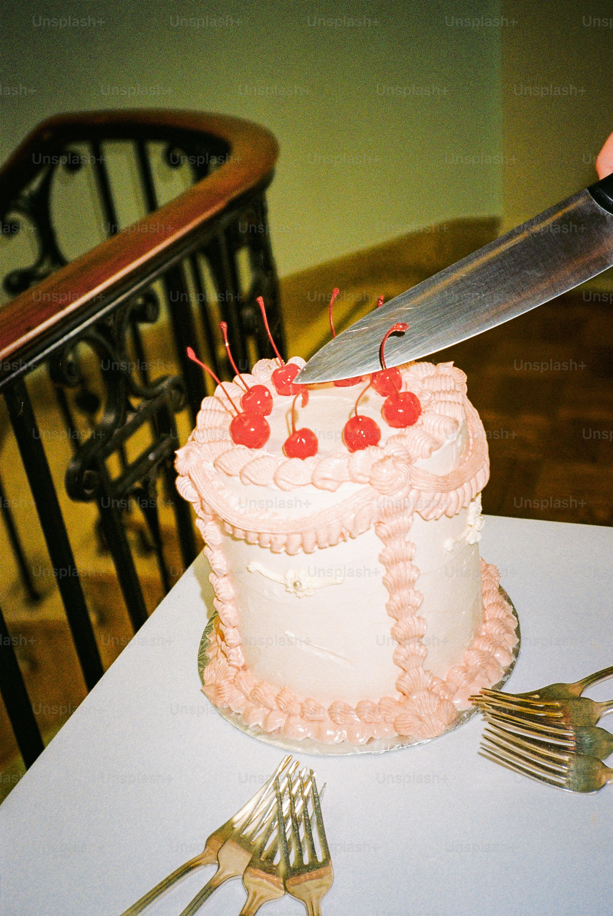 A knife cuts a cake decorated with cherries.